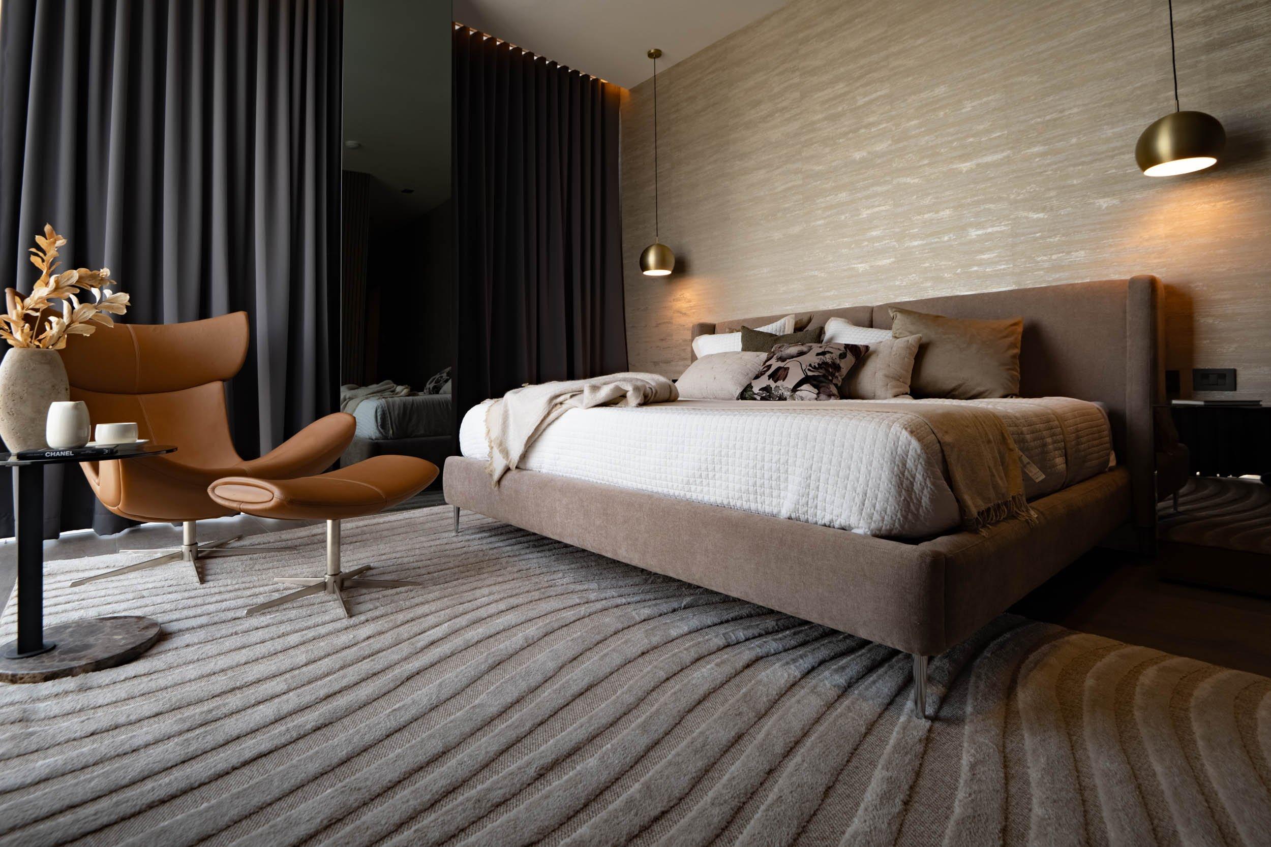 Chambre moderne avec lit rembourré, fauteuil en cuir et suspensions au-dessus de la tête de lit.