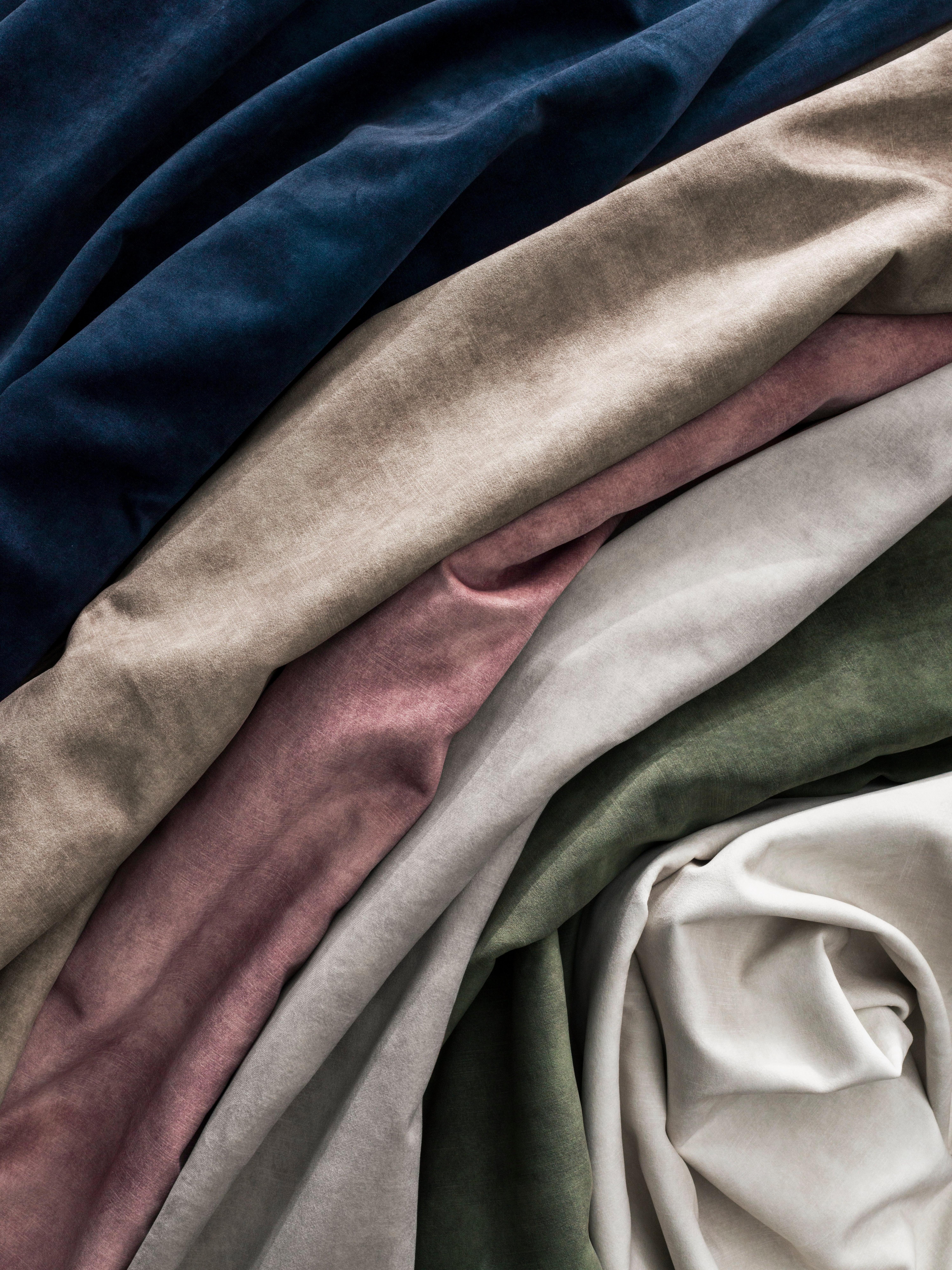 A close-up of layered velvet fabric in deep blue, beige, mauve, gray, green, and off-white, showcasing soft texture and rich tones.