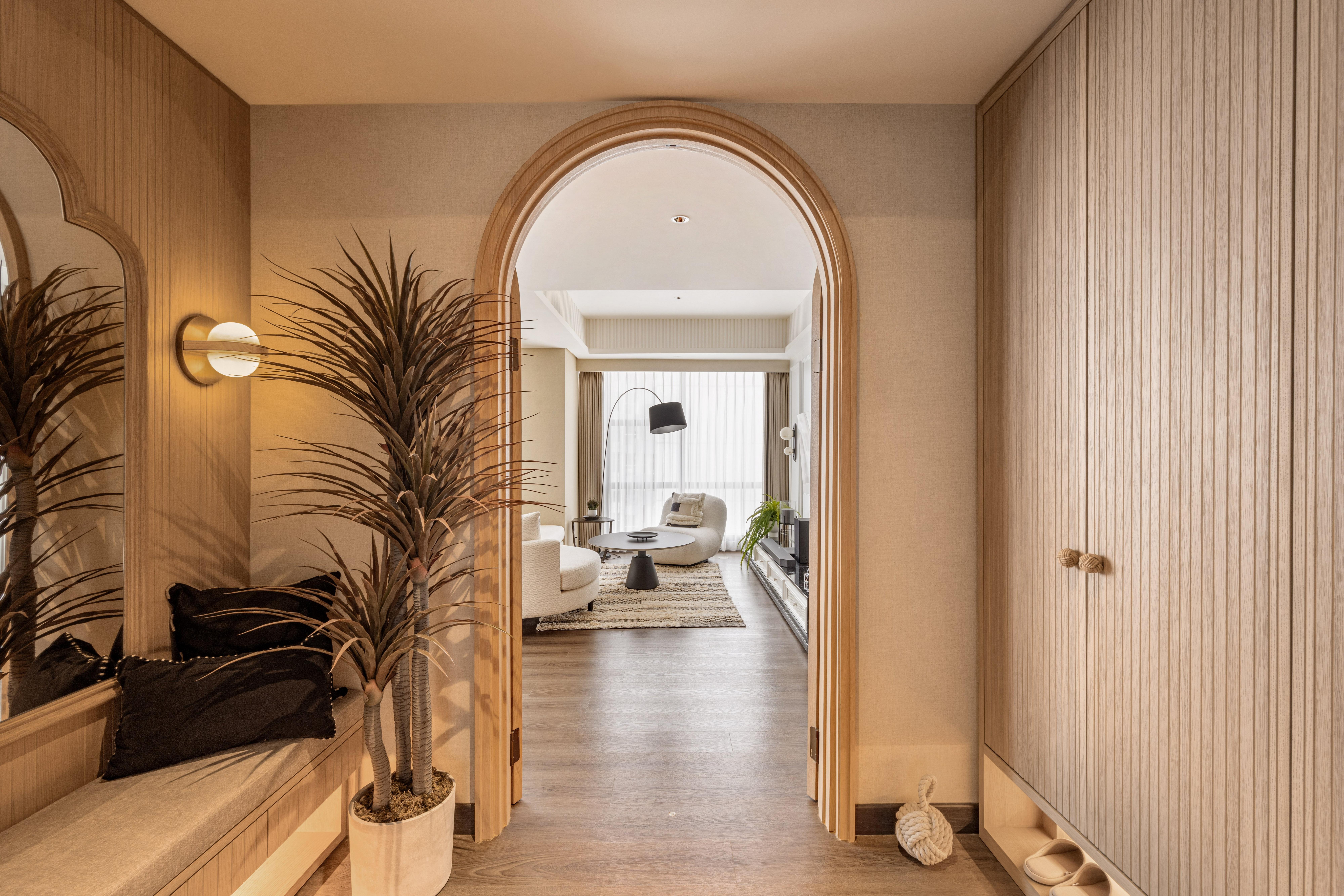 Arched hallway with built-in bench, potted plant and ribbed wardrobe, leading to a lounge.