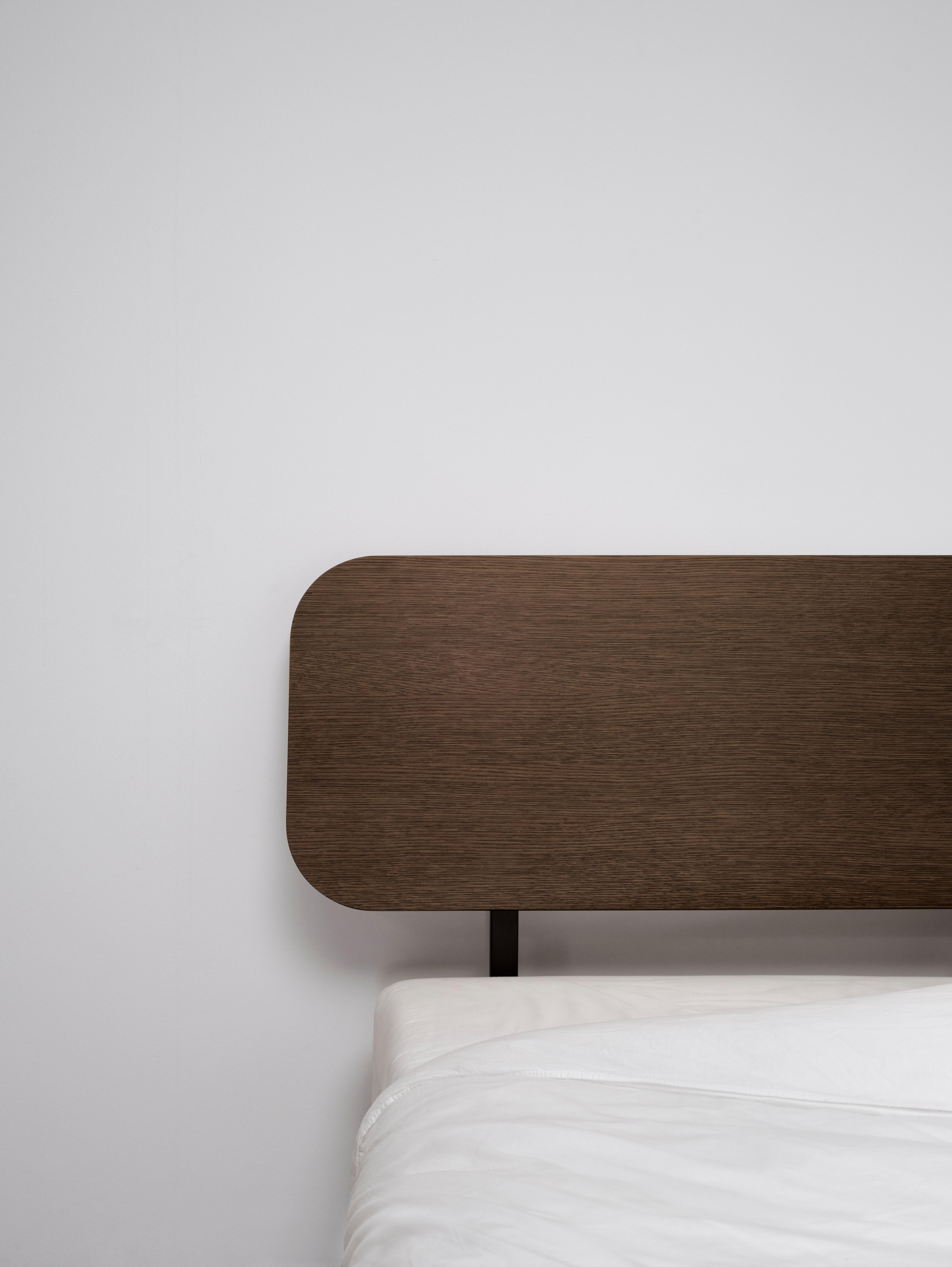 Wooden headboard with rounded corners, white bedding partially visible.