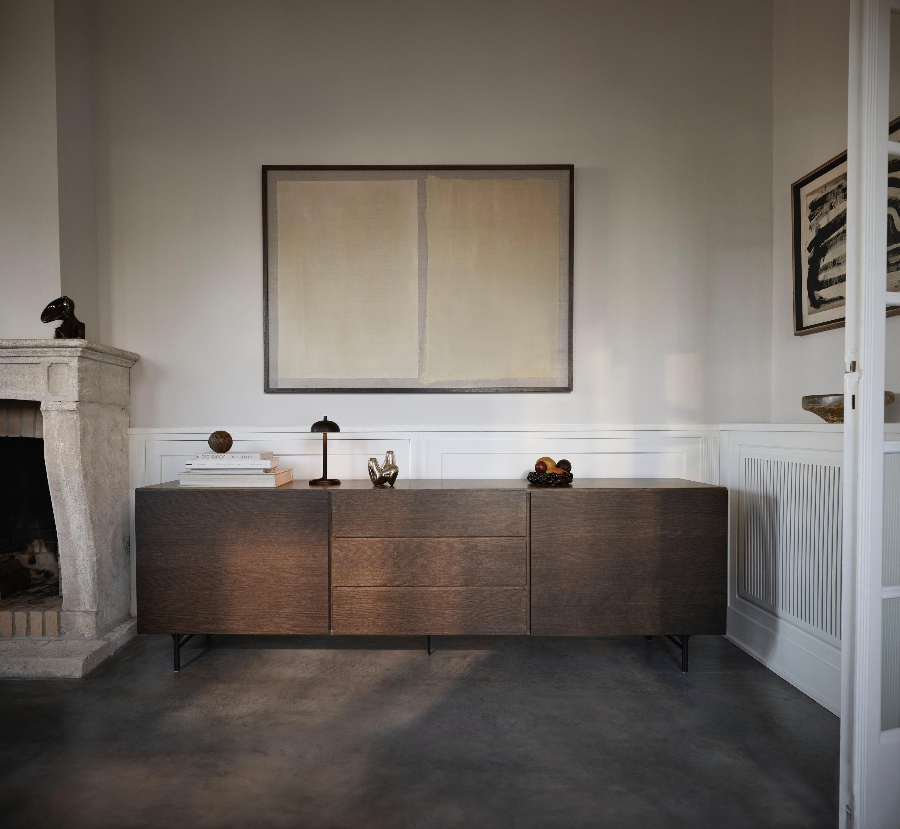 Modern sideboard with art above, set near a fireplace. Decorative items and books on top.