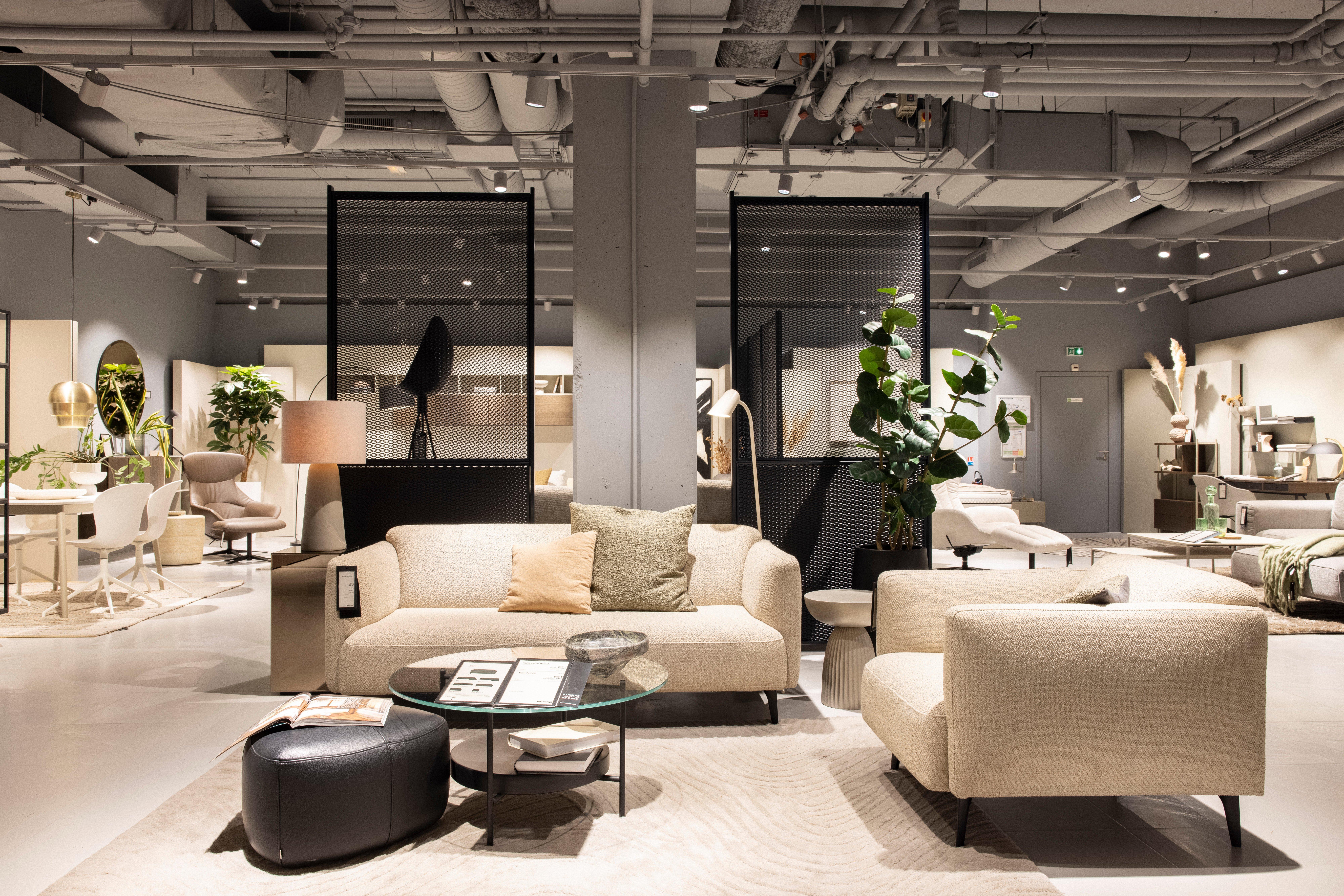 Moderne Möbelausstellung mit beigen Sofas, Couchtisch, Pflanzen und dekorativen Elementen.