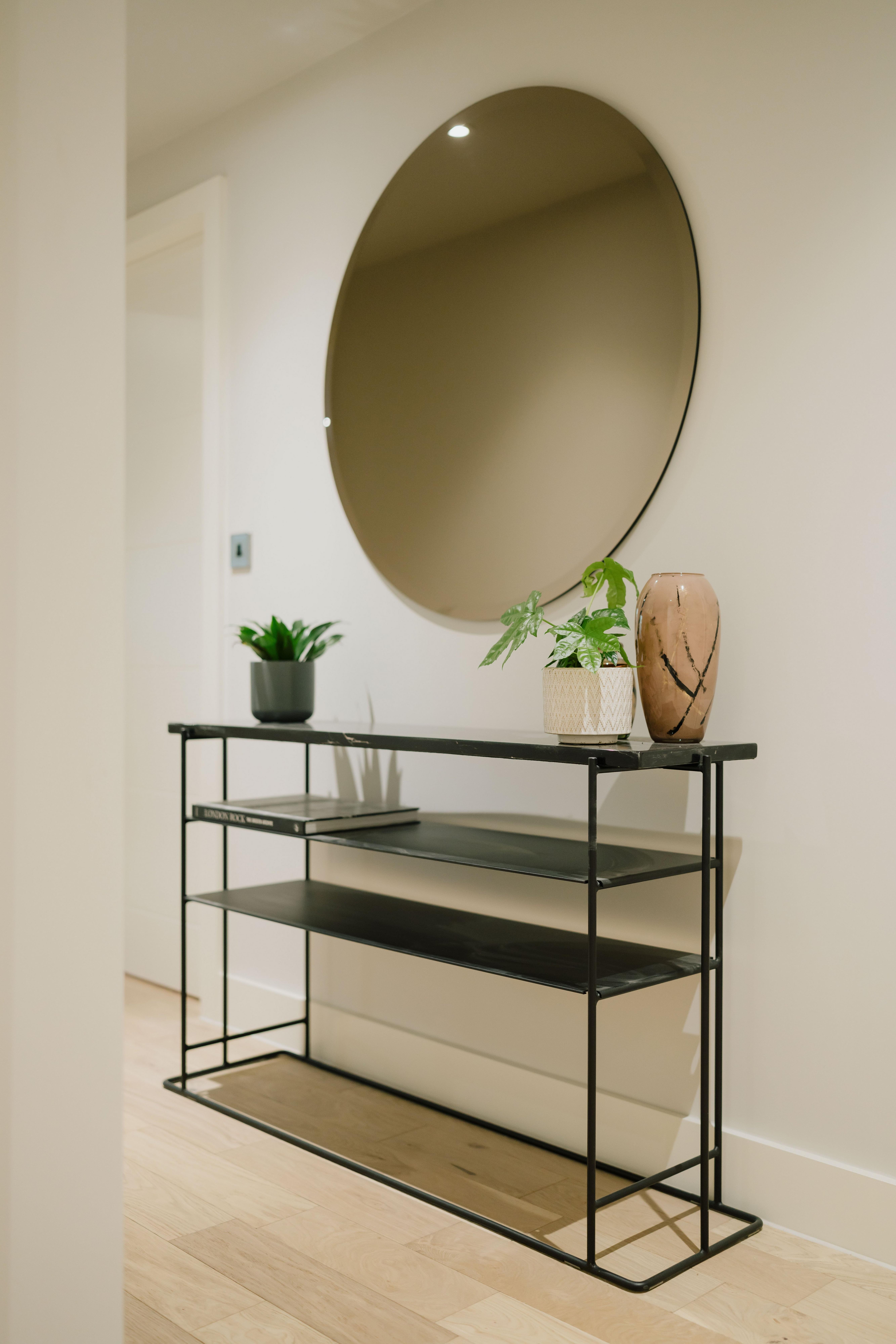Minimalist console table with plants and vase under a large round mirror.