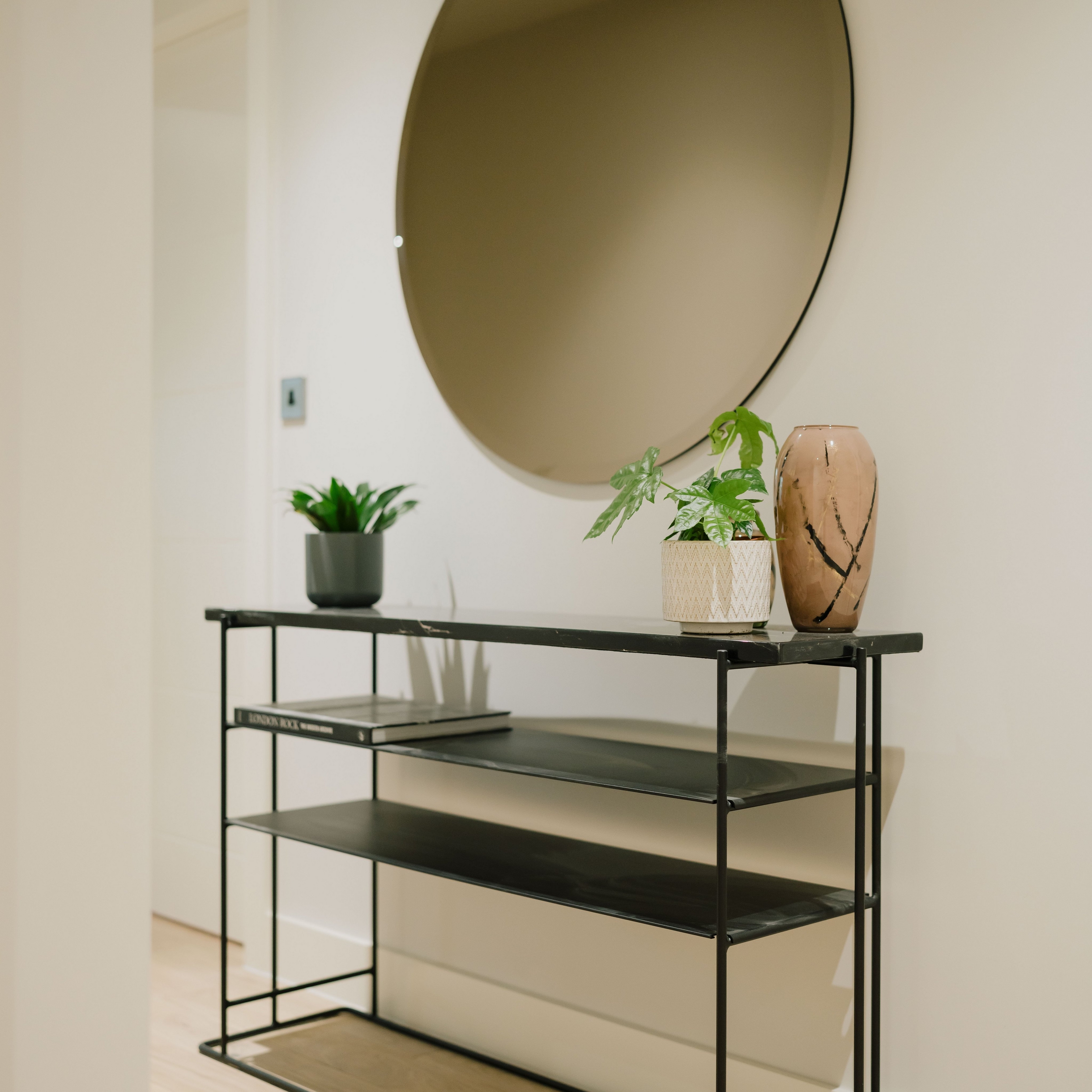 Minimalist console table with plants and vase under a large round mirror.