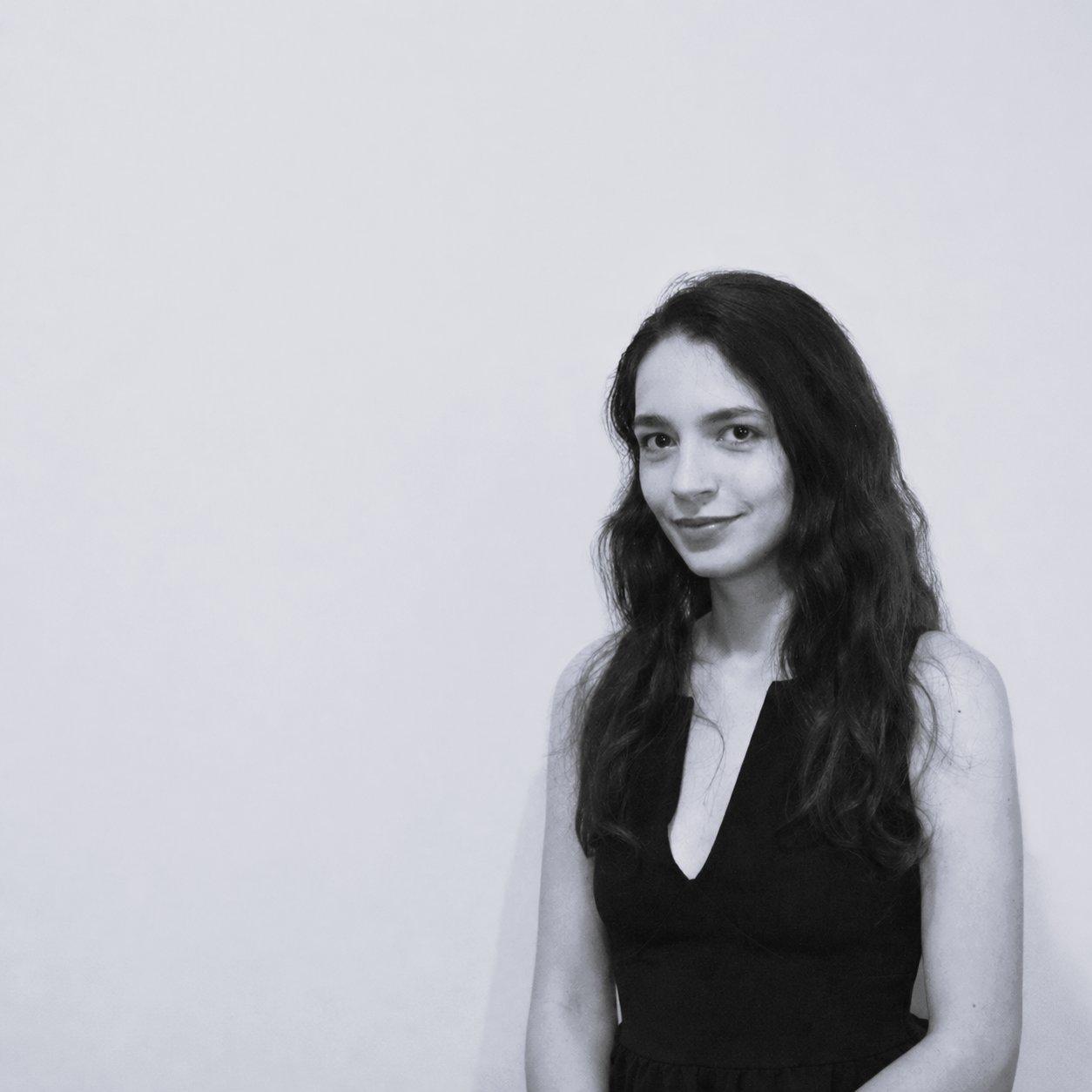 Woman with long hair wearing a sleeveless black V-neck dress, posing for a portrait.