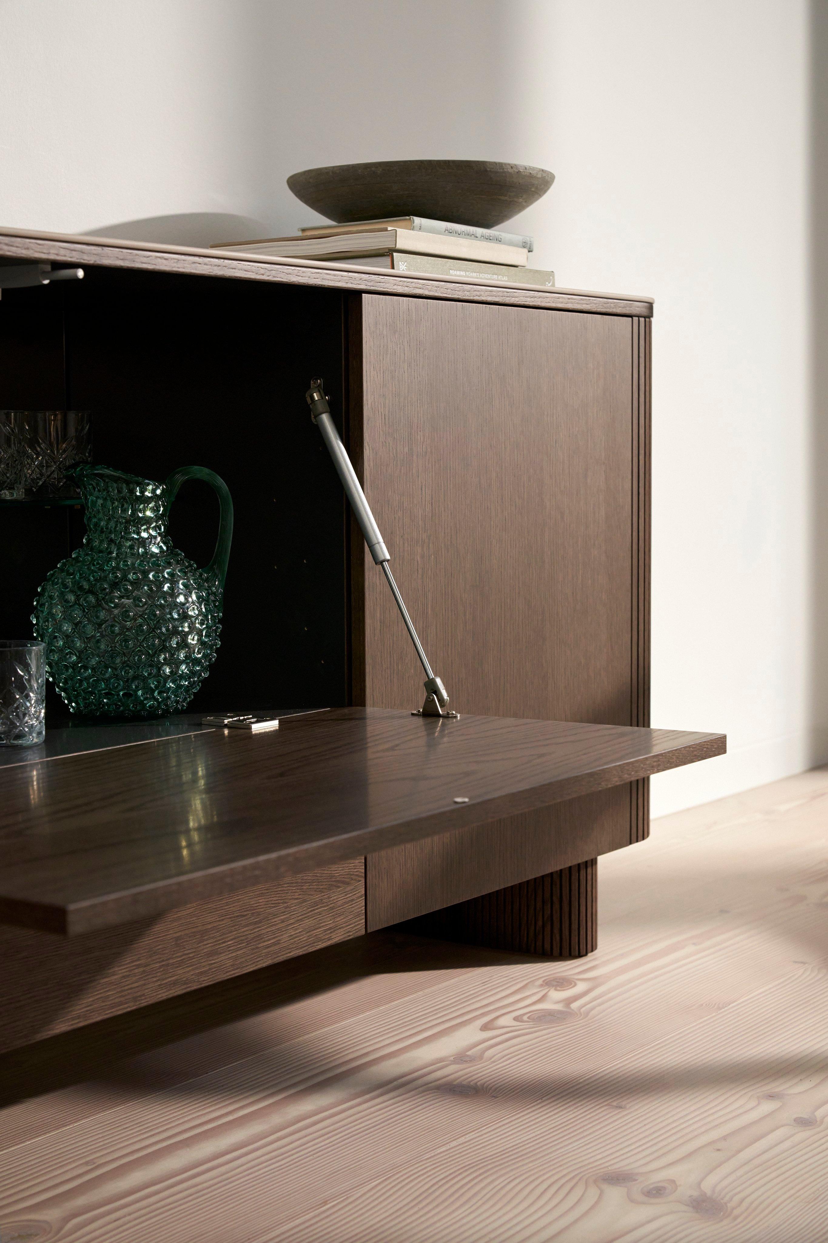 Armoire en bois avec porte ouverte, carafe en verre à l'intérieur. Livres et bol sur le dessus.