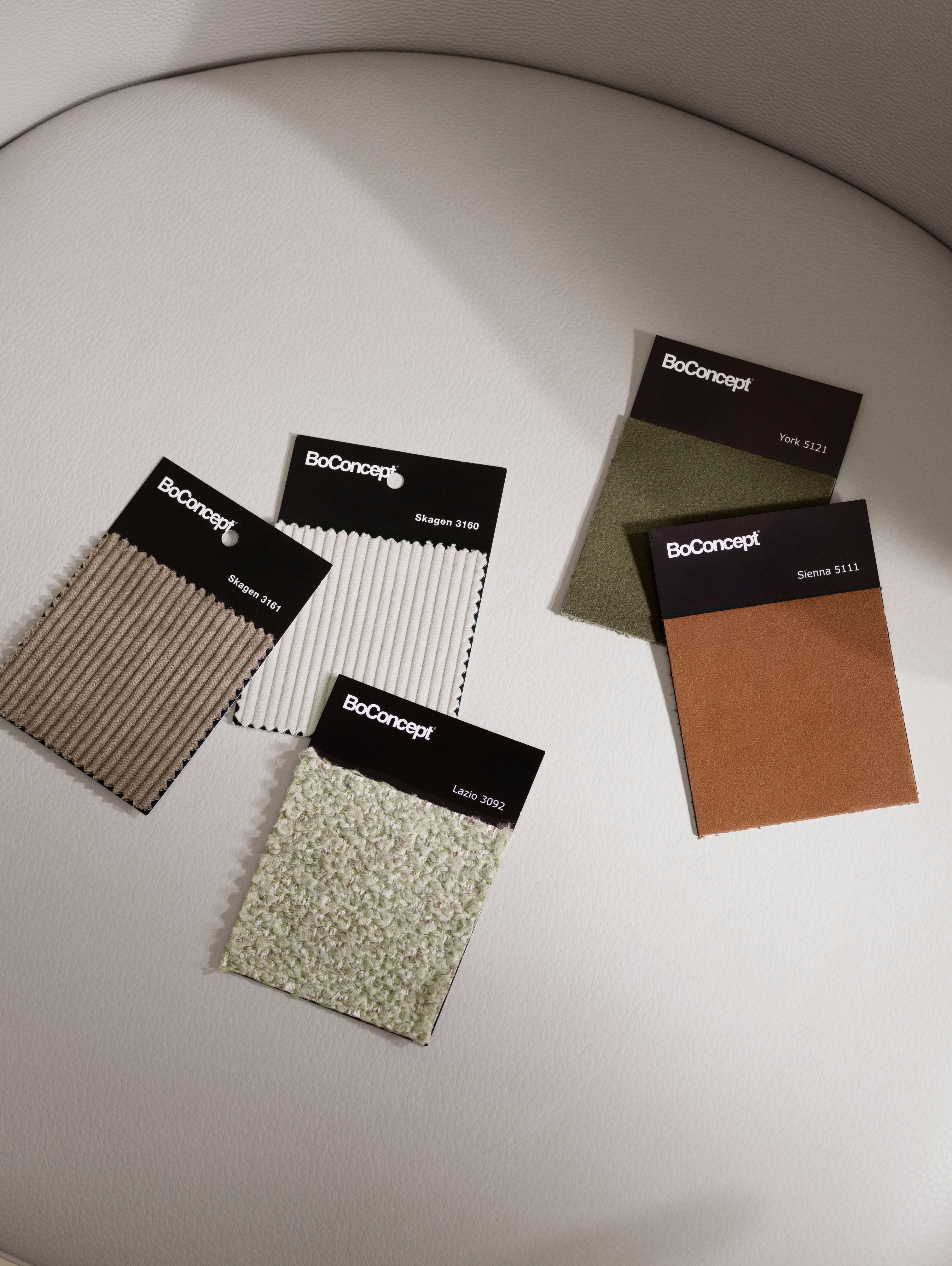 Échantillons de tissu BoConcept sur une chaise blanche, présentant diverses textures et couleurs.