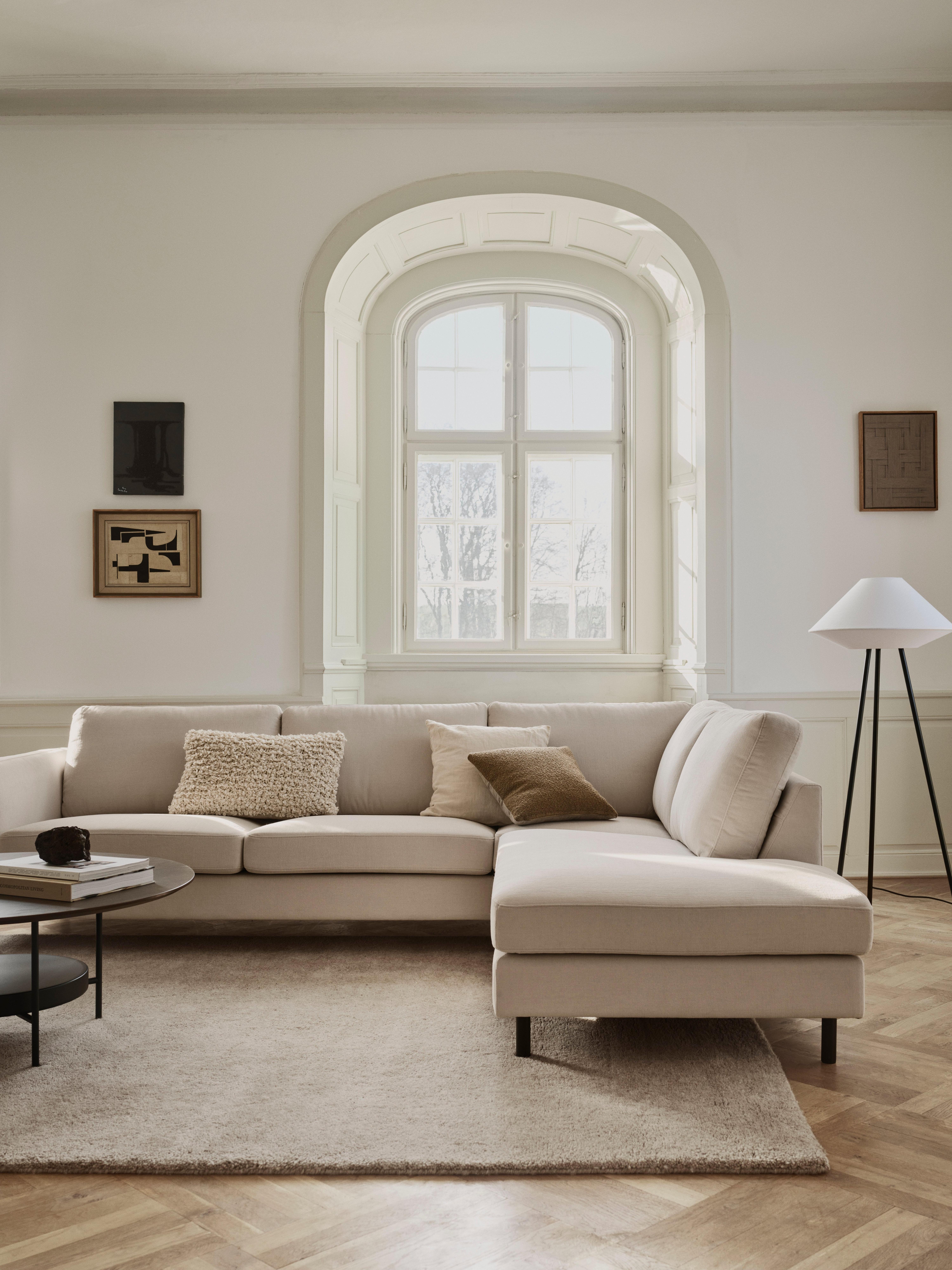 Beiges Ecksofa mit Kissen im Wohnzimmer, neben Stehlampe und Couchtisch.