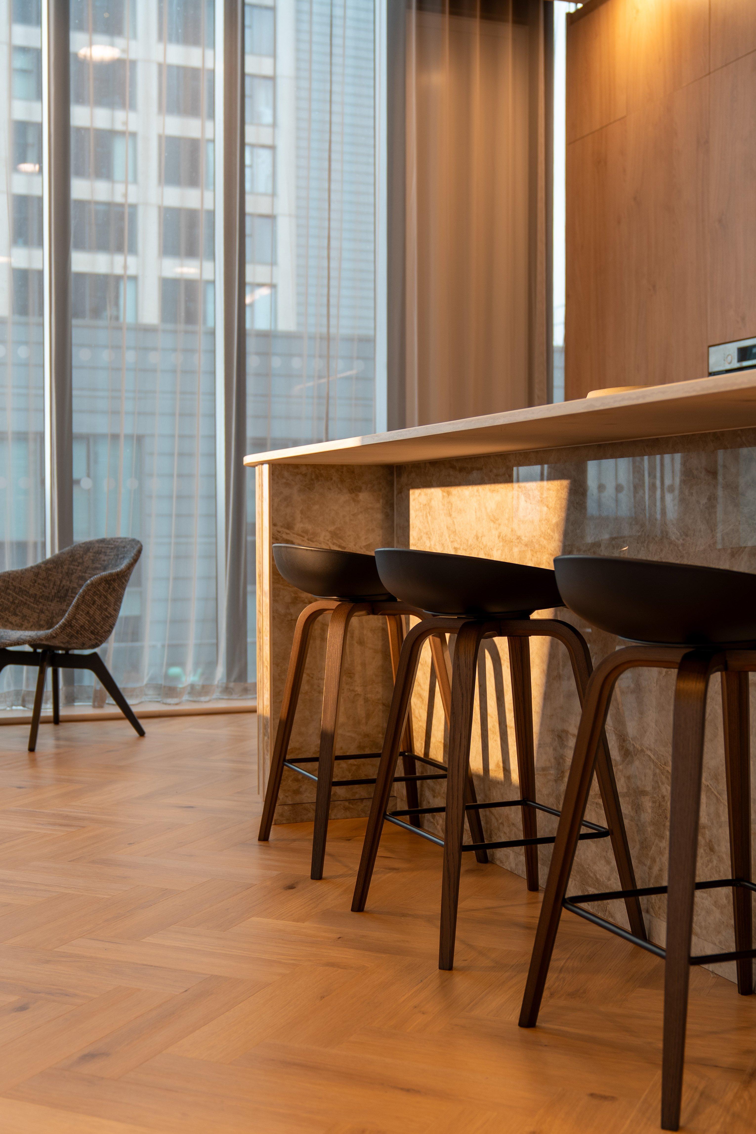 Tres taburetes de bar negros con patas de madera junto a una isla de cocina moderna.