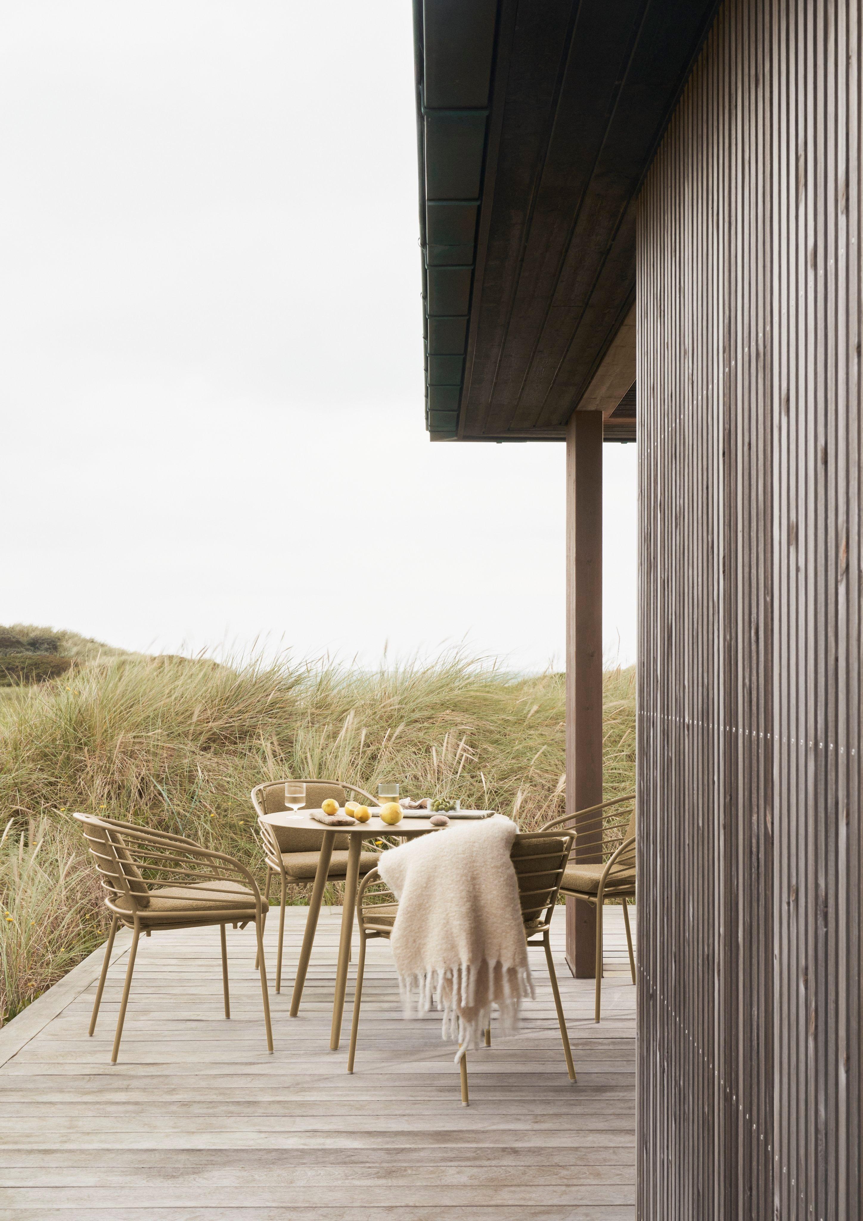 Holzterrasse mit Tisch, vier Stühlen und Decke, umgeben von hohen Gräsern.