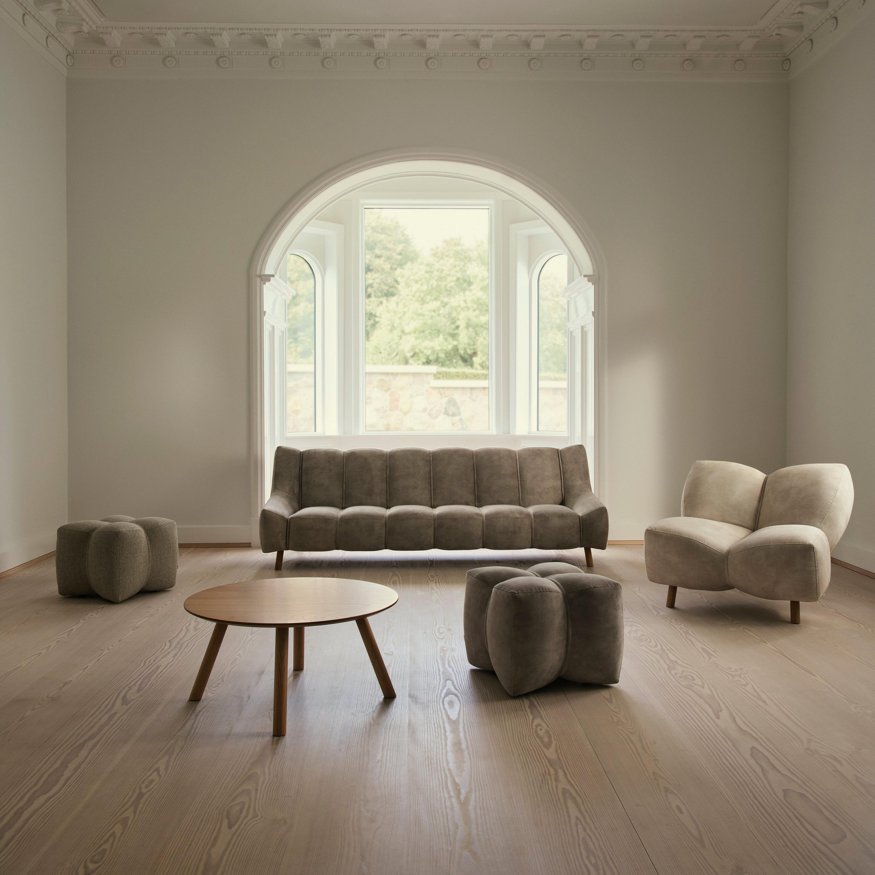 Minimalist living room with grey sofa, armchair, round table, and ottomans. Large arched window.