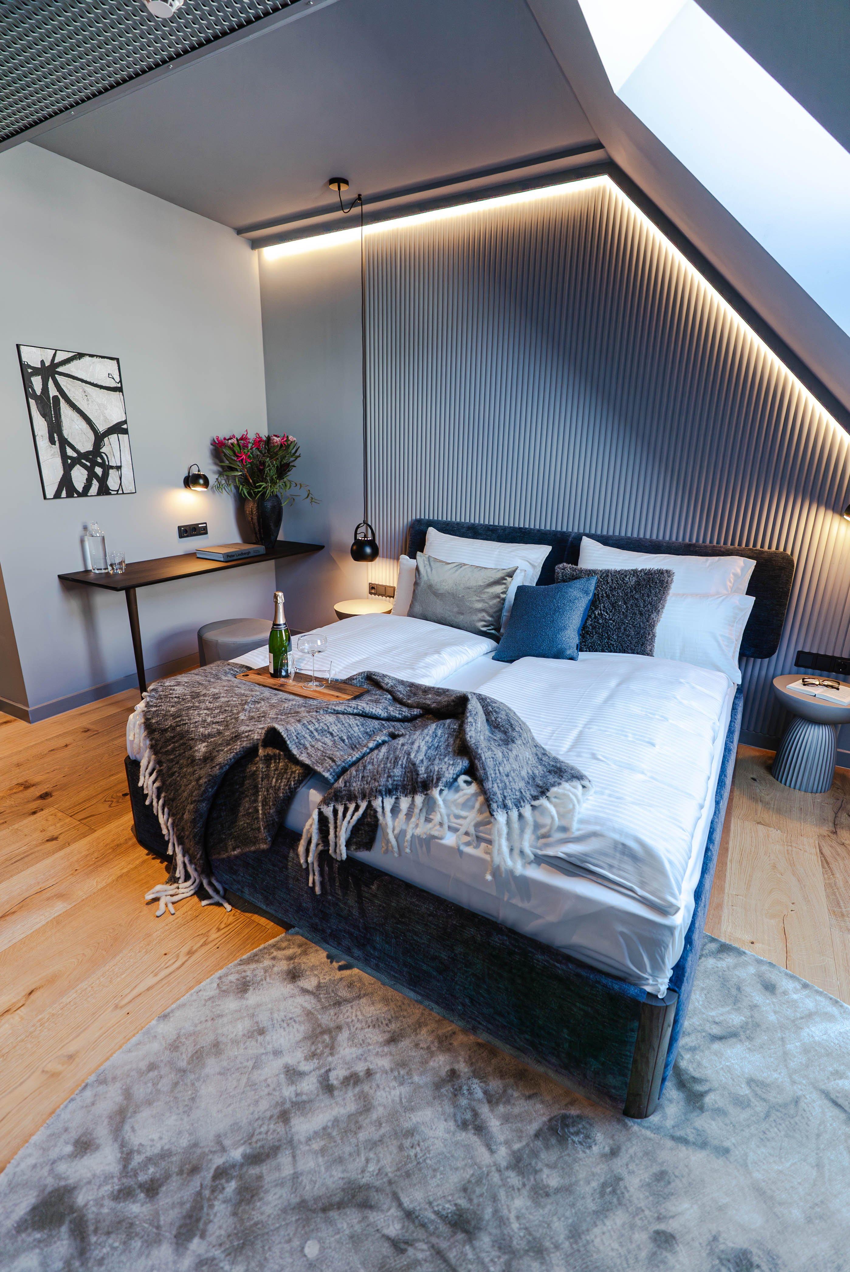 Chambre moderne avec lit double, plaid gris, table de chevet, et décoration florale.