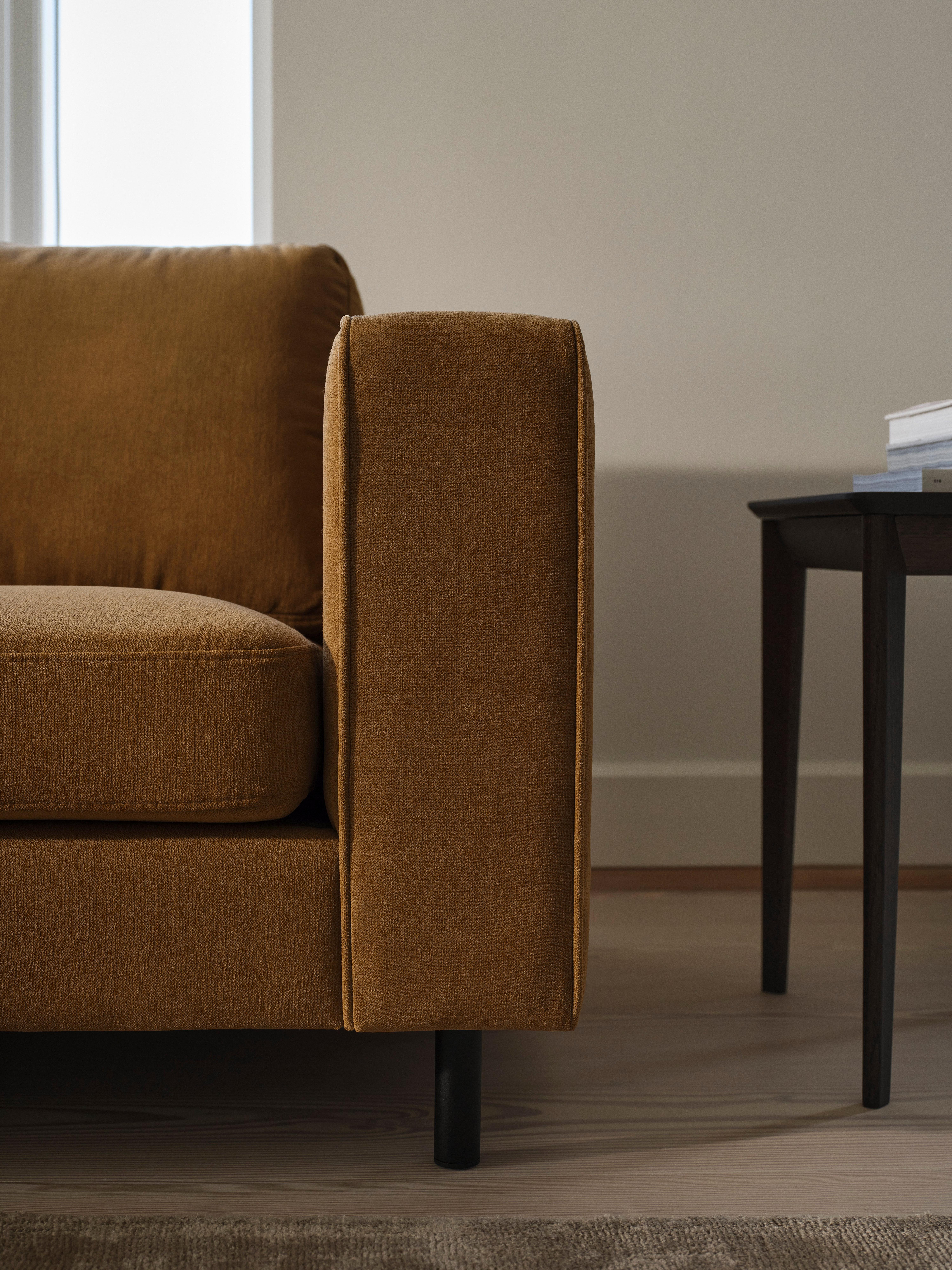 Braunes Sofa mit Armlehne, daneben ein dunkler Beistelltisch mit Büchern.