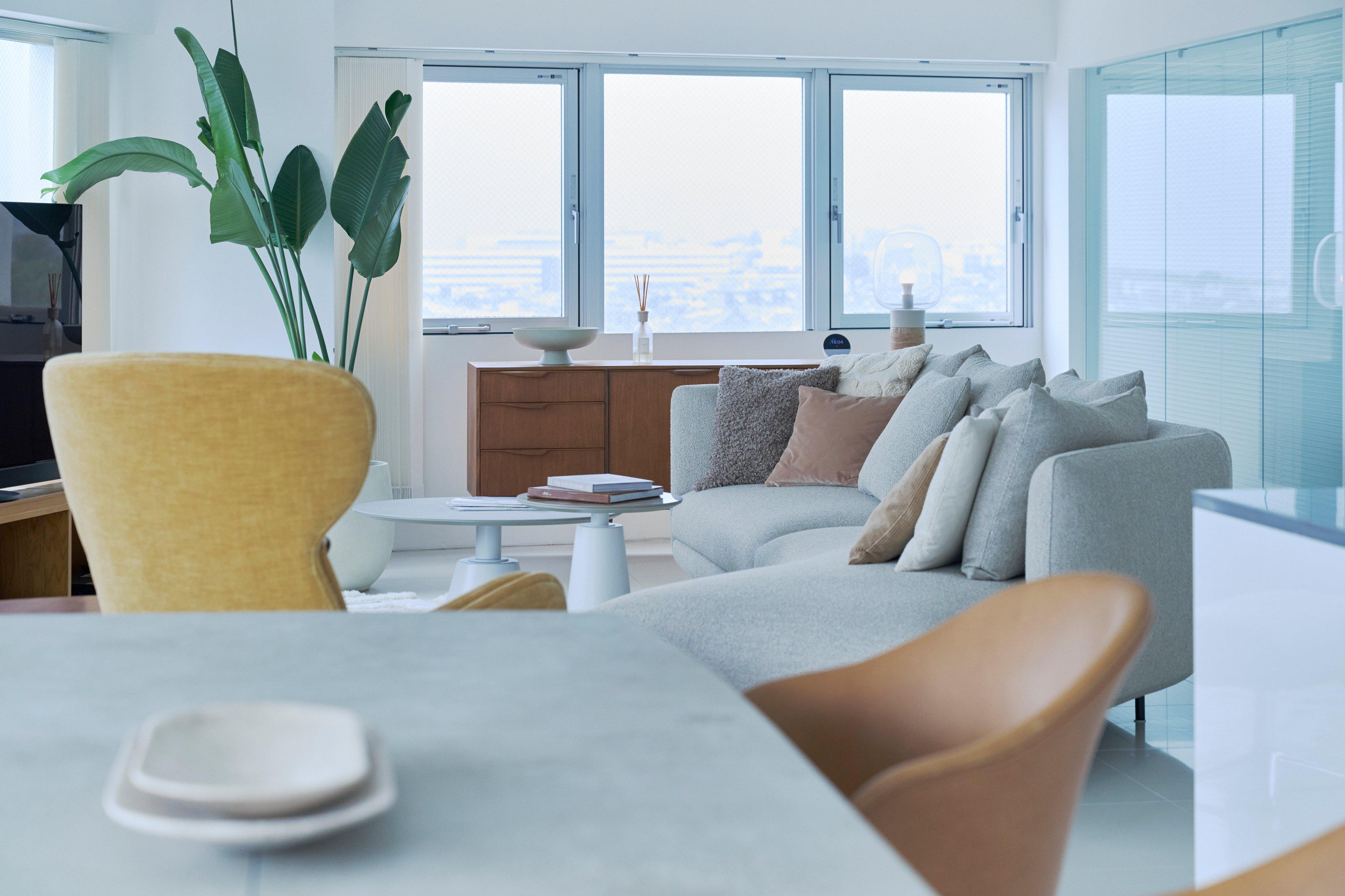 Modern living room with grey corner sofa, coffee table and cushions by large windows.