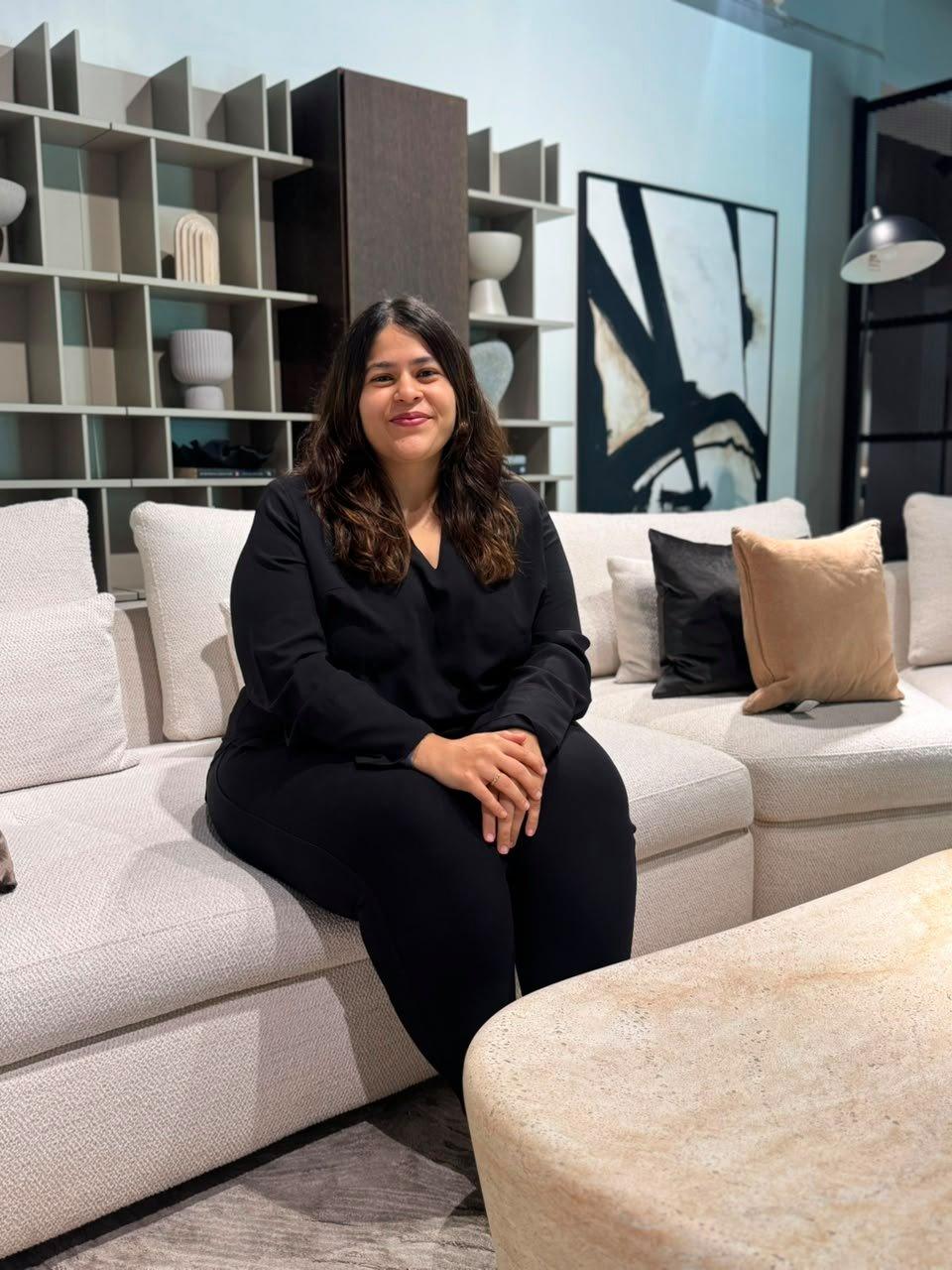 Woman sitting on a light grey corner sofa with mixed cushions in a living room showroom.
