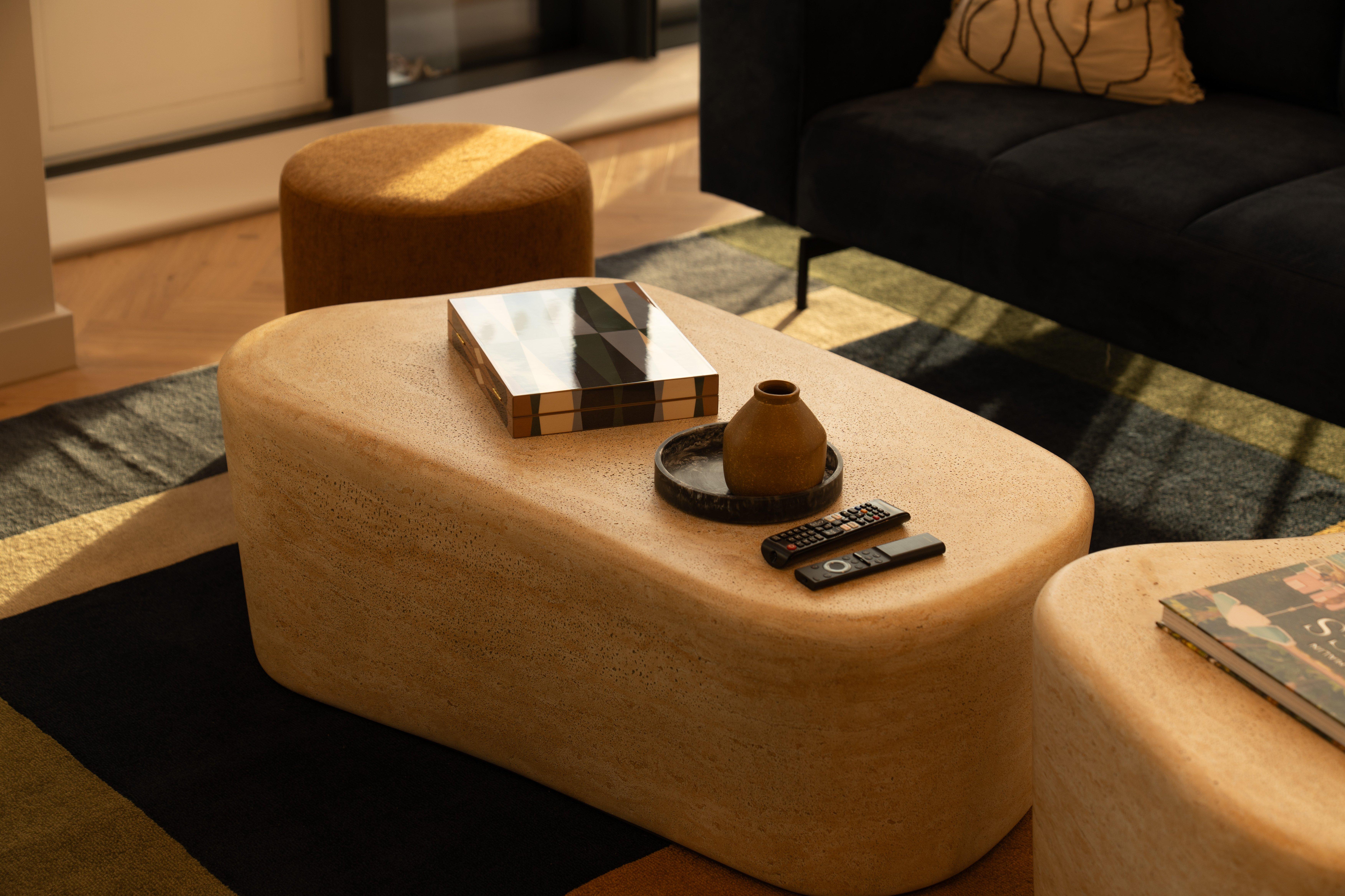 Mesa de centro beige con bandeja y jarrón, dos mandos a distancia y caja decorativa.