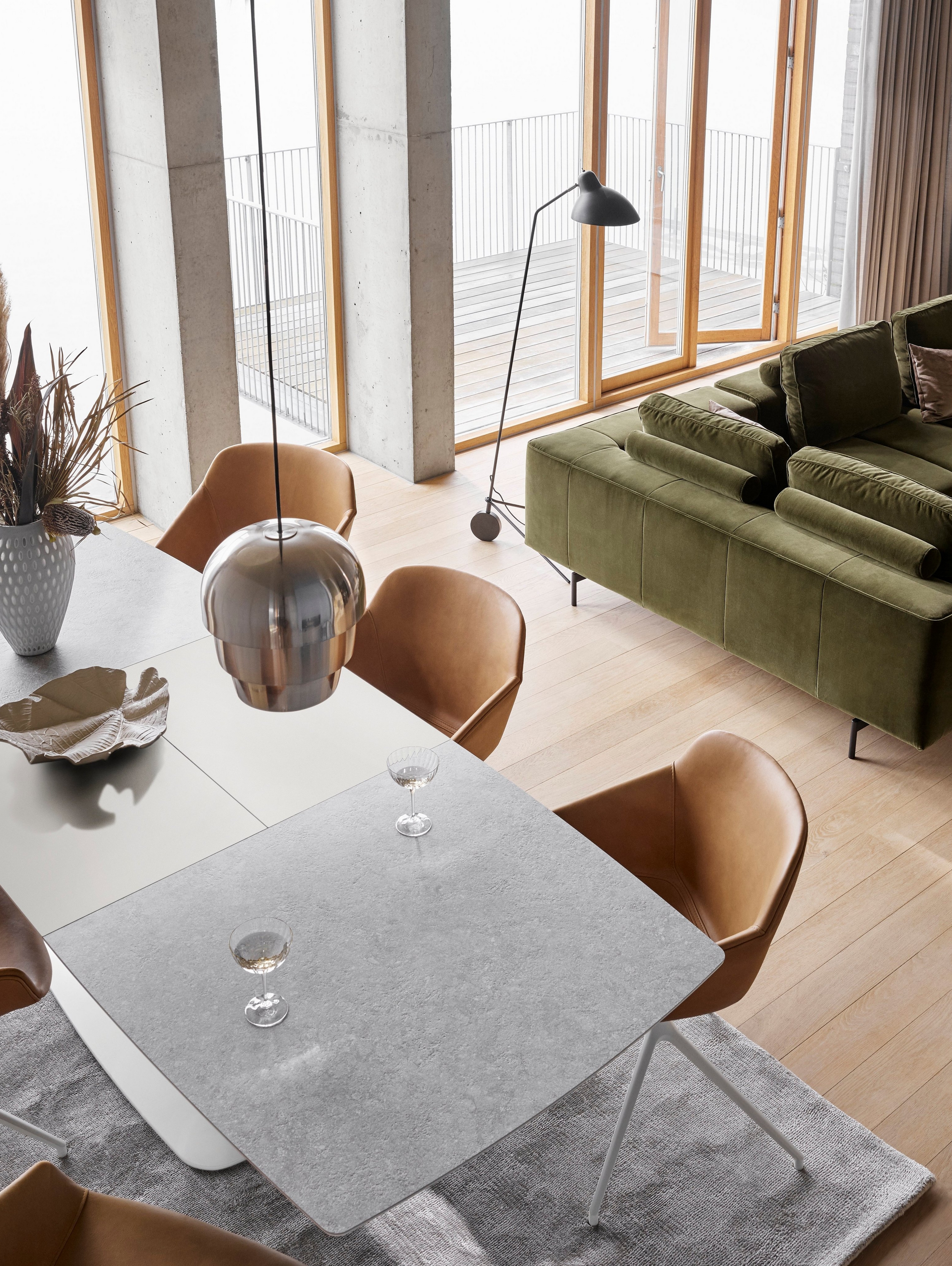 Le canapé d’angle Amsterdam avec module lounging en velours vert olive, avec la table de repas Alicante, la table basse Madrid et la chaise Vienna en cuir York cognac.