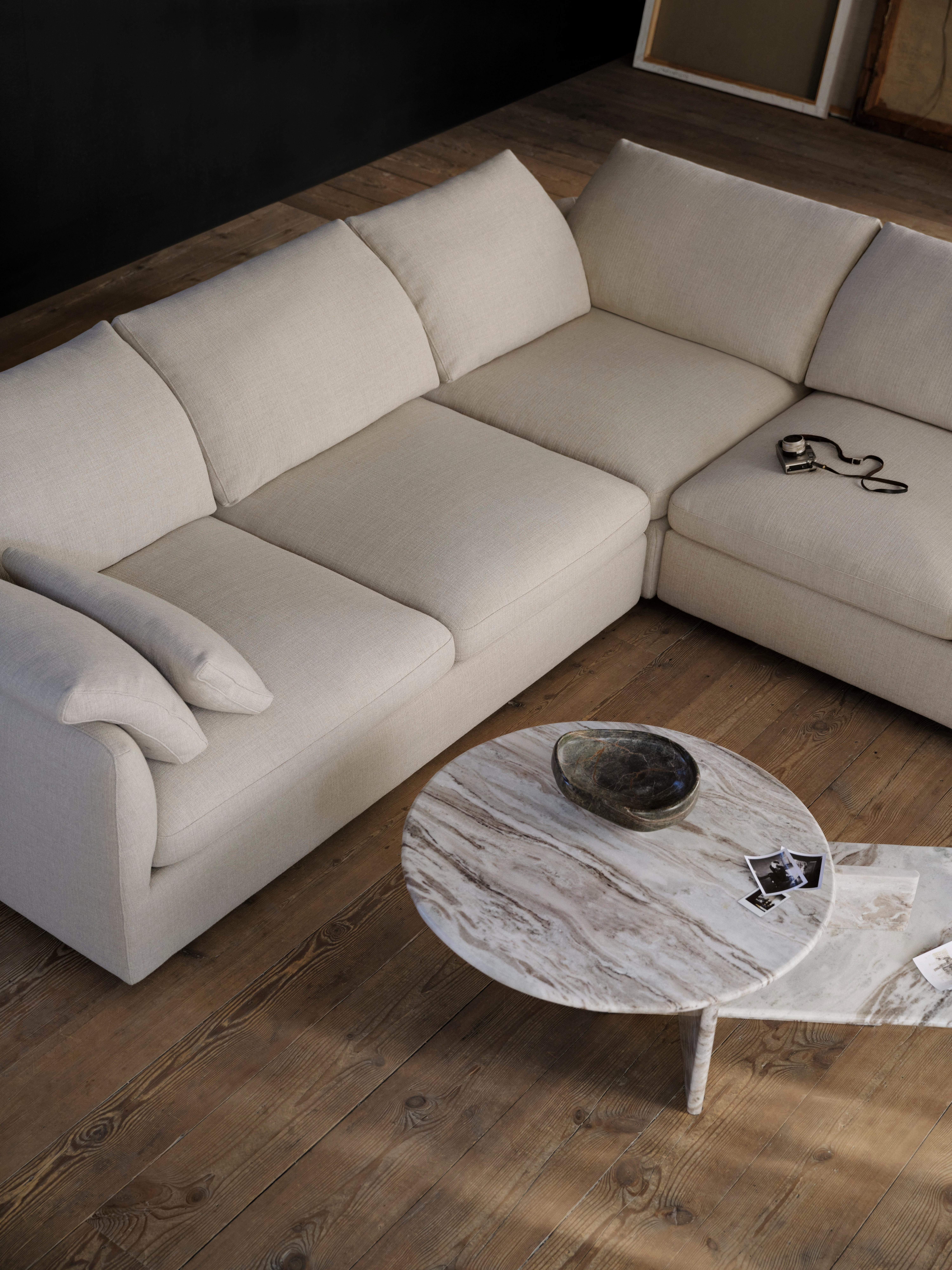 Modern living area with a white Bellagio sofa and pouf. Natural coloured throw and pillows accent the furniture. A book lies open on the sofa.