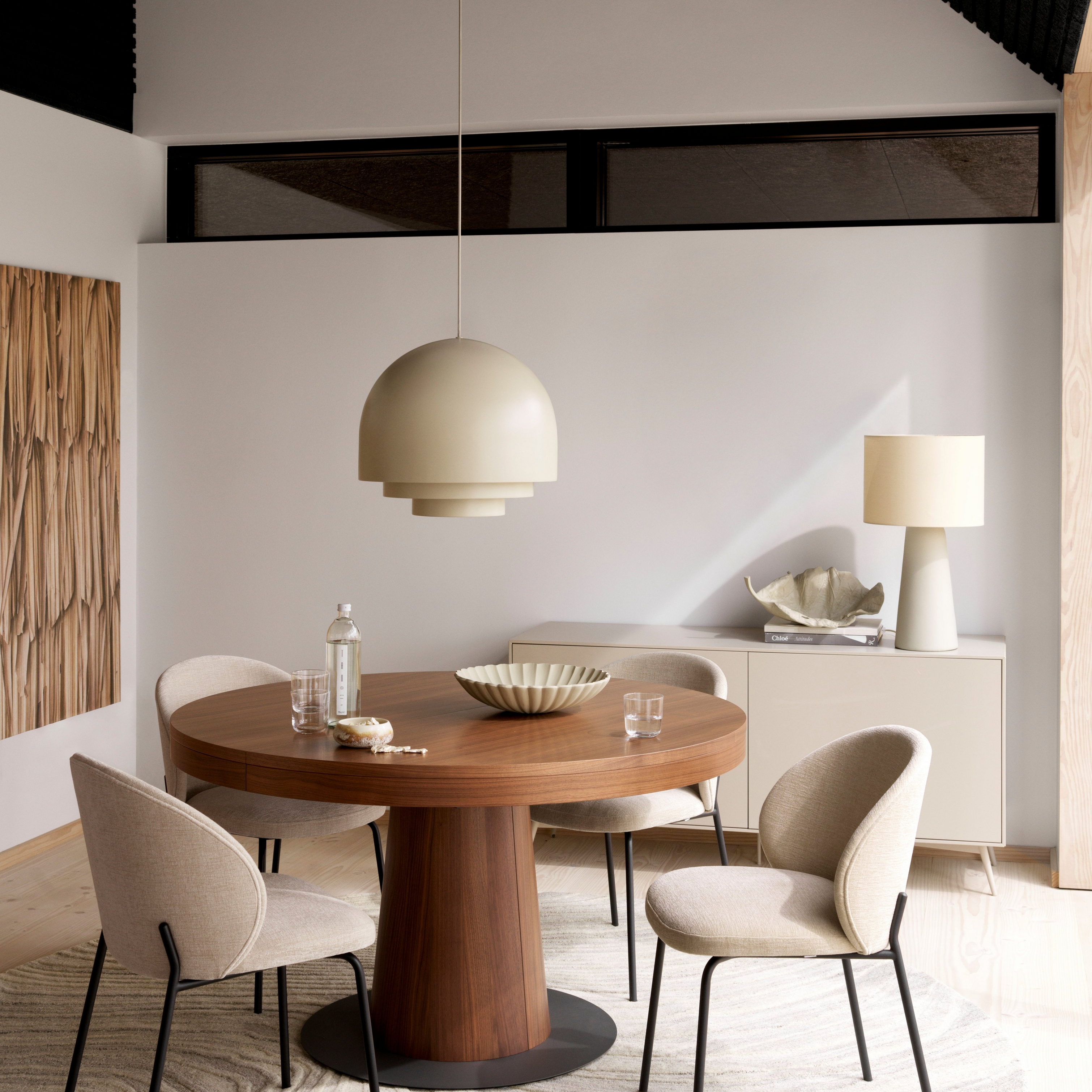 Sala de jantar moderna com mesa redonda Granada em madeira, cadeiras Princeton beges, pendente de luz e tapete creme.