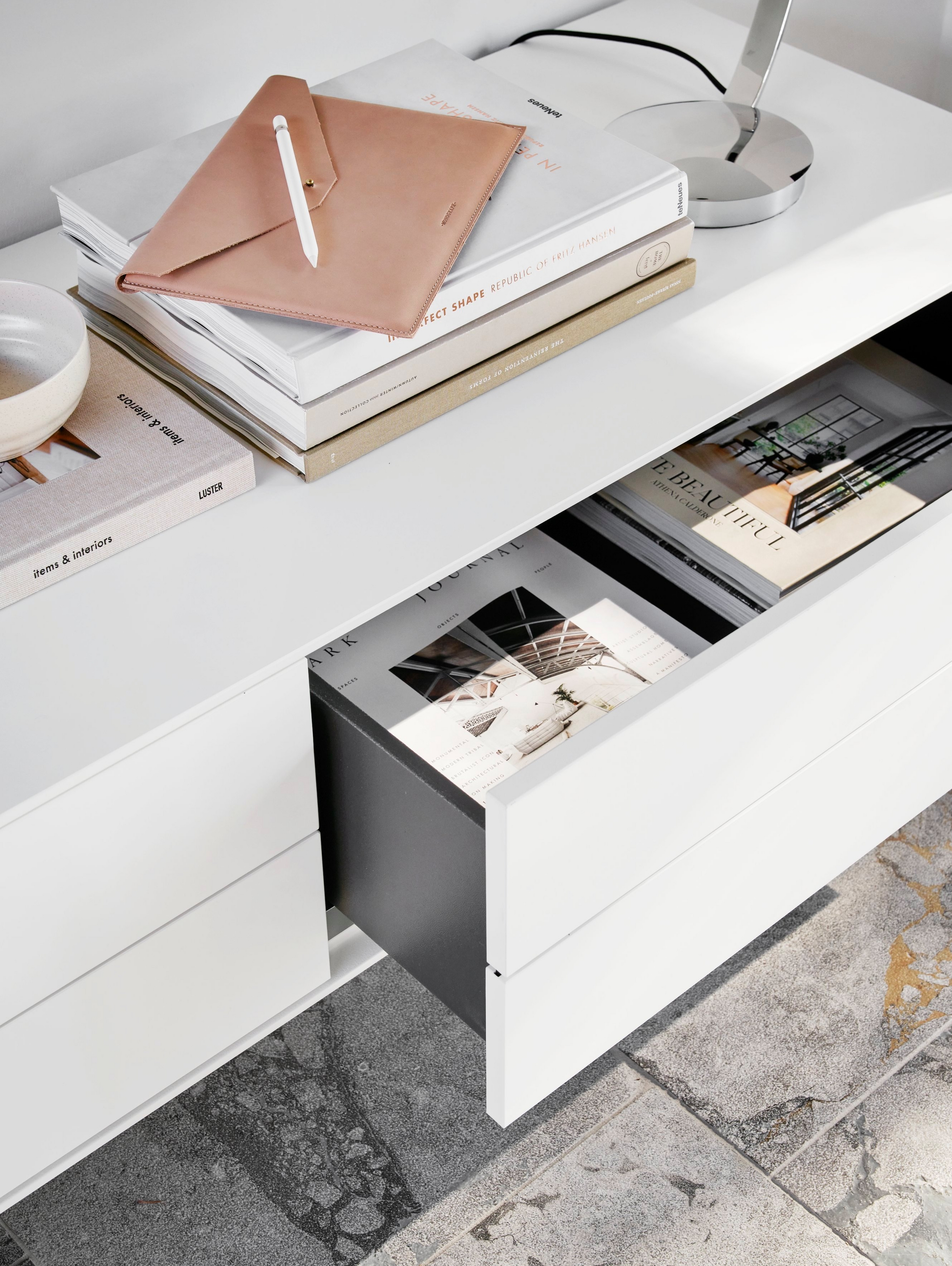 Desk with books, a leather folder and an open drawer revealing magazines