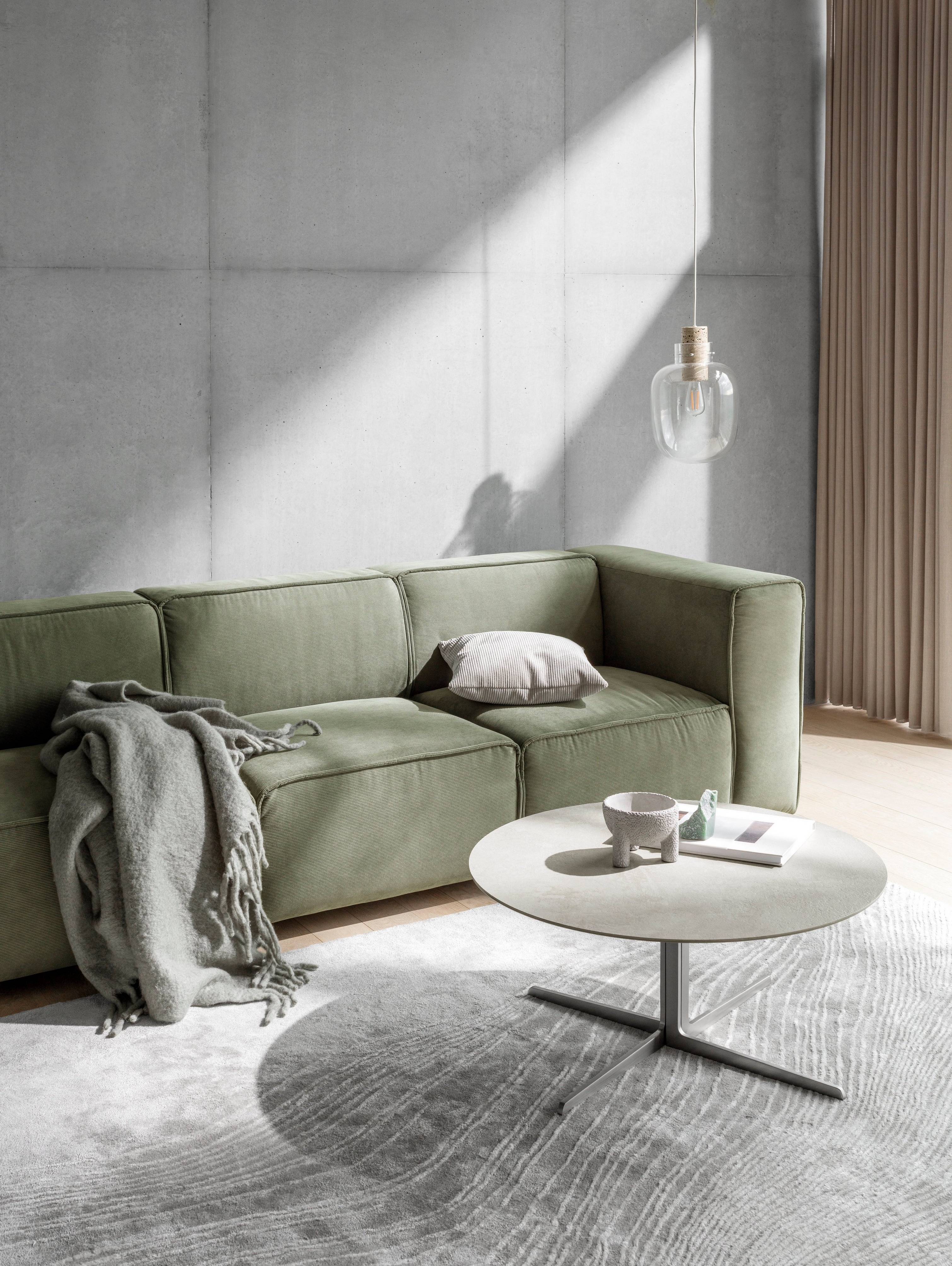 The Carmo sofa in a nicly sunlit room with a pillow and a rug placed on the seats.