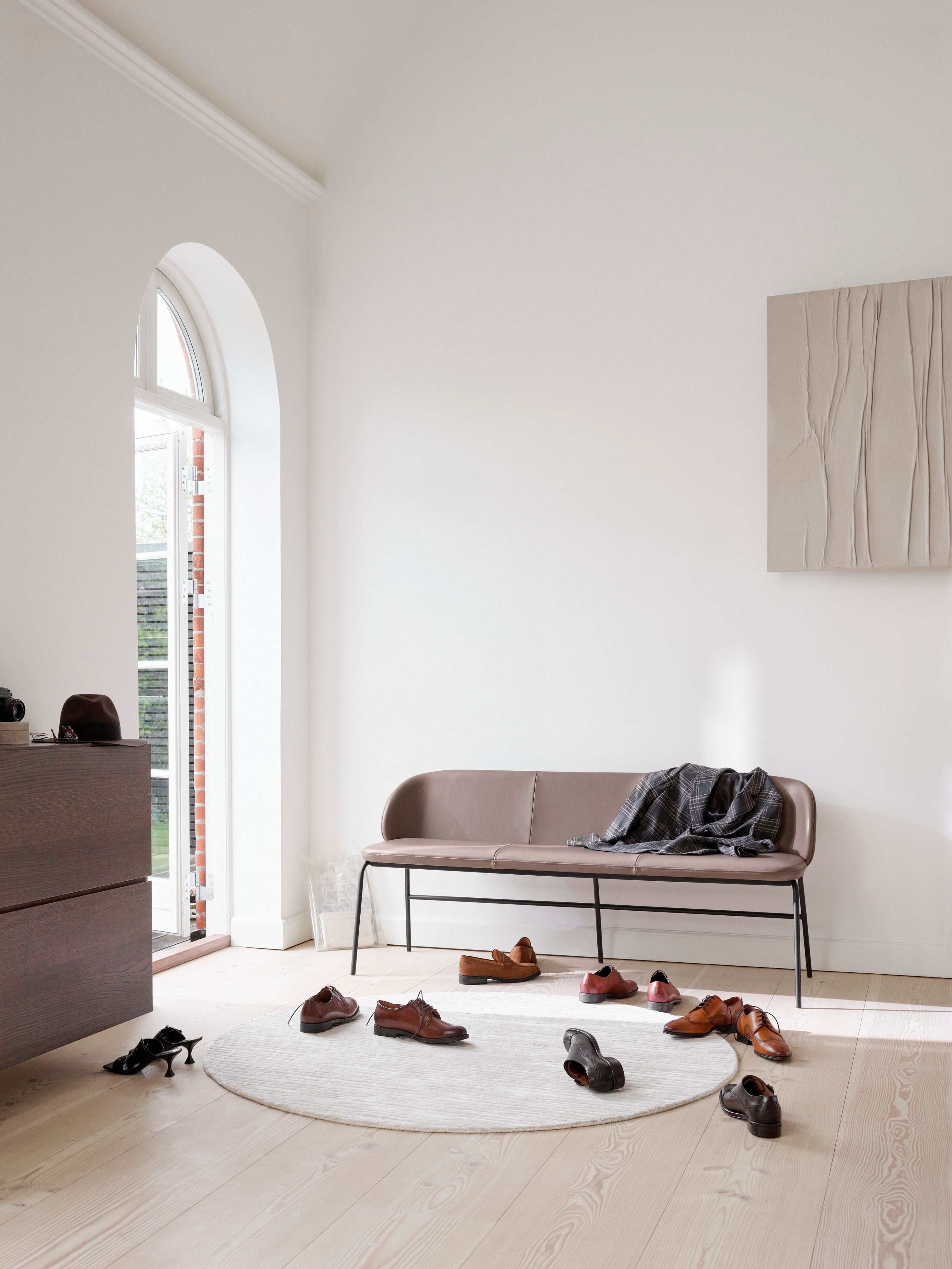 Lederbank in einem hellen Raum mit Rundbogenfenster, Schuhen auf dem Boden und Holzkunst.