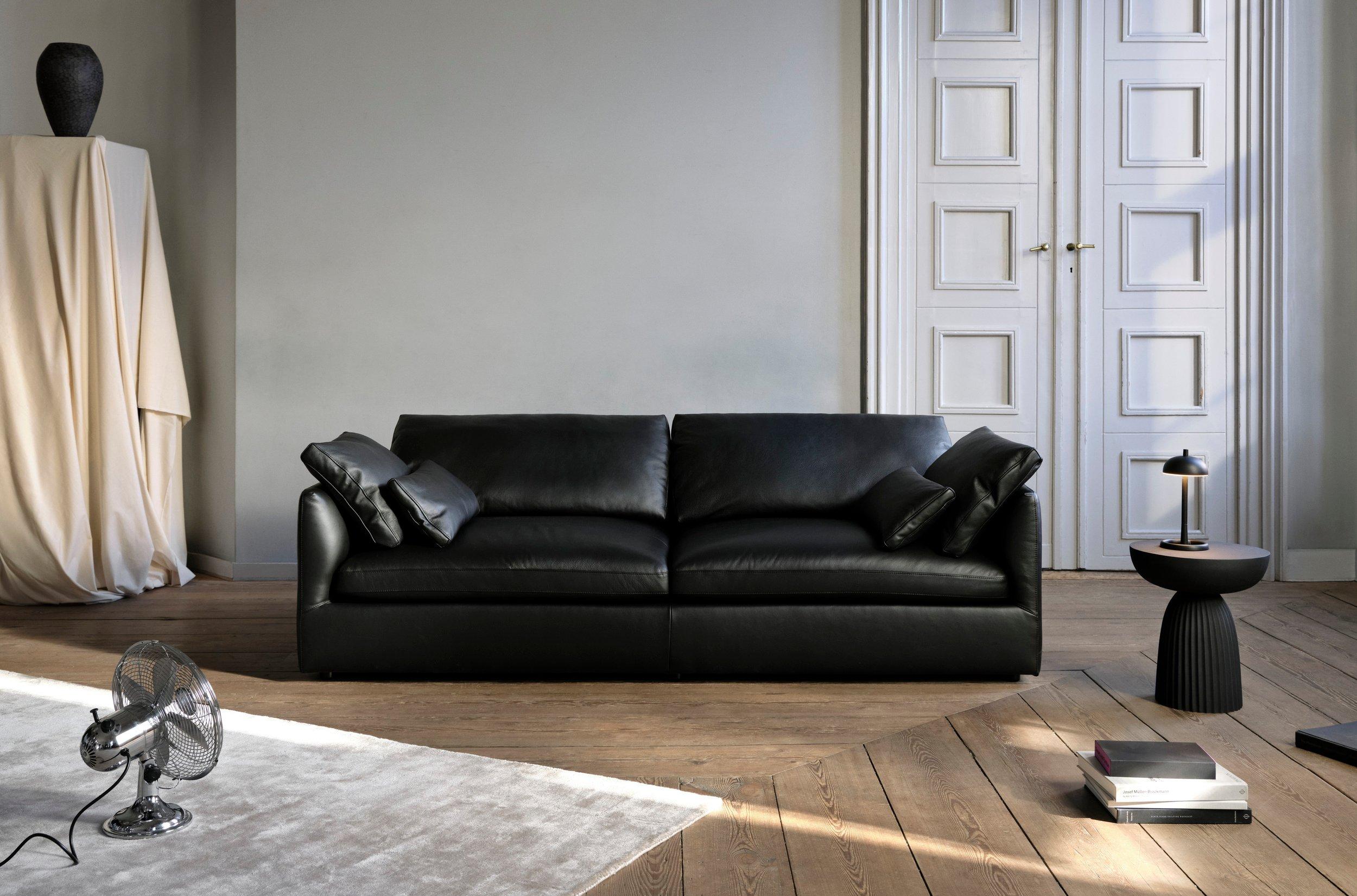 Black Paris table lamp on black Expose side table beside black sofa; Rubble vase on draped pedestal in classic interior.