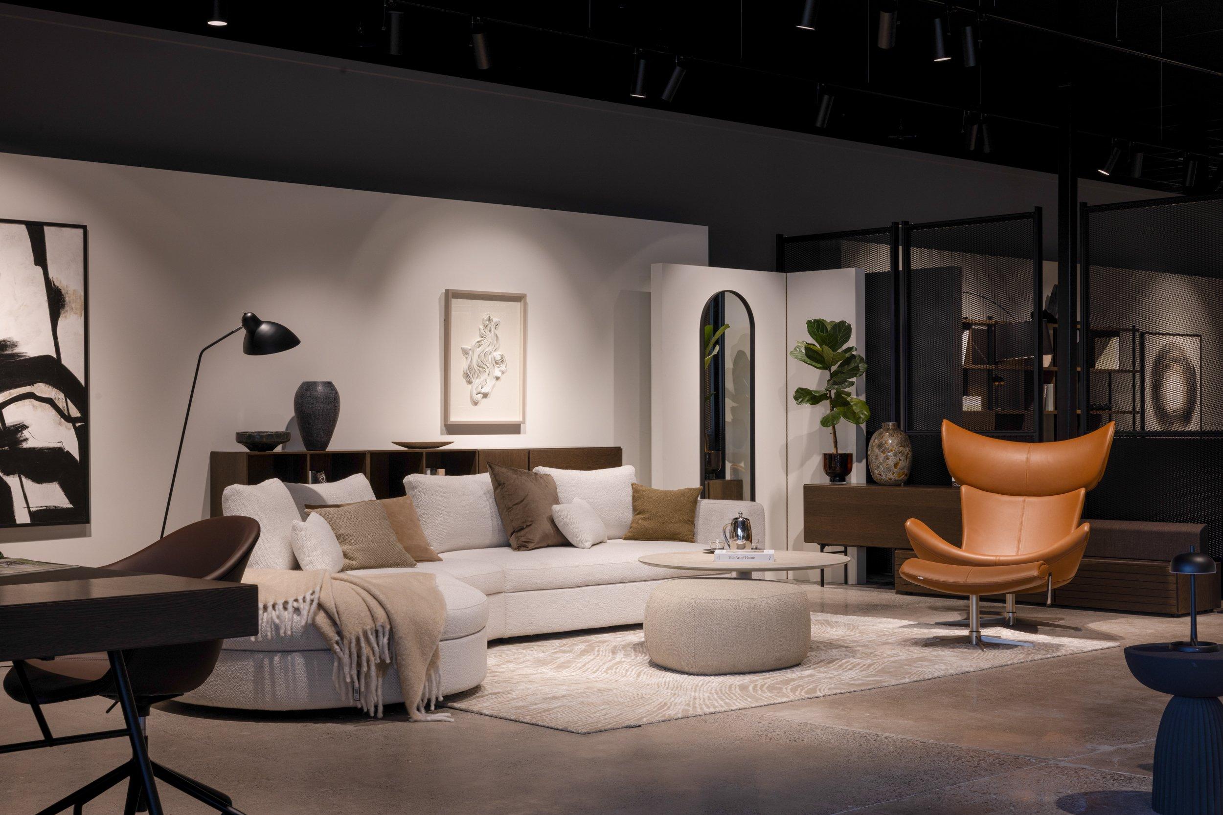 Indrettet stue med stor lys sofa, lavt sofabord og brun lænestol.