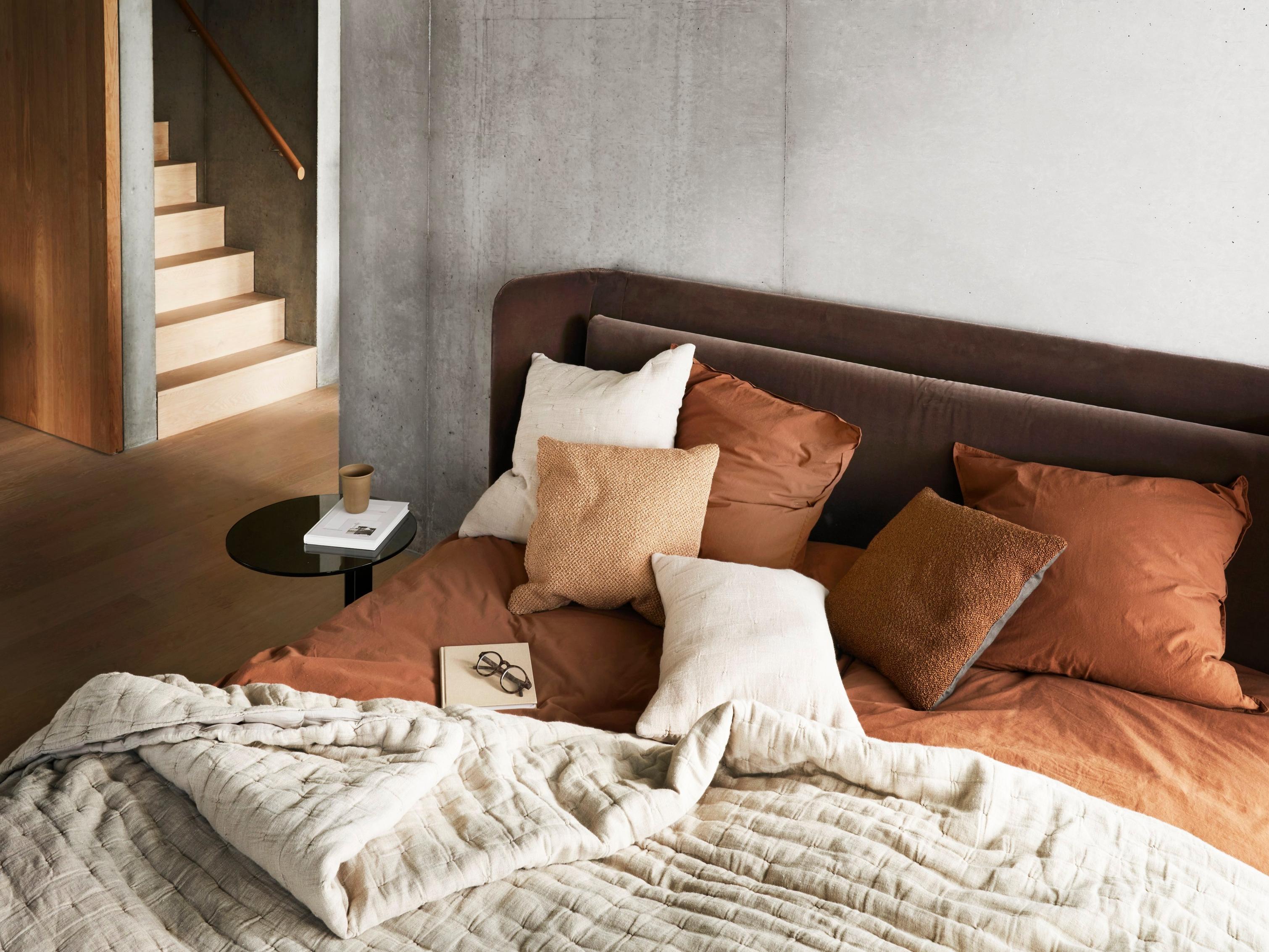 Modern bedroom with soft bedding and neutral tones, featuring a small side table.
