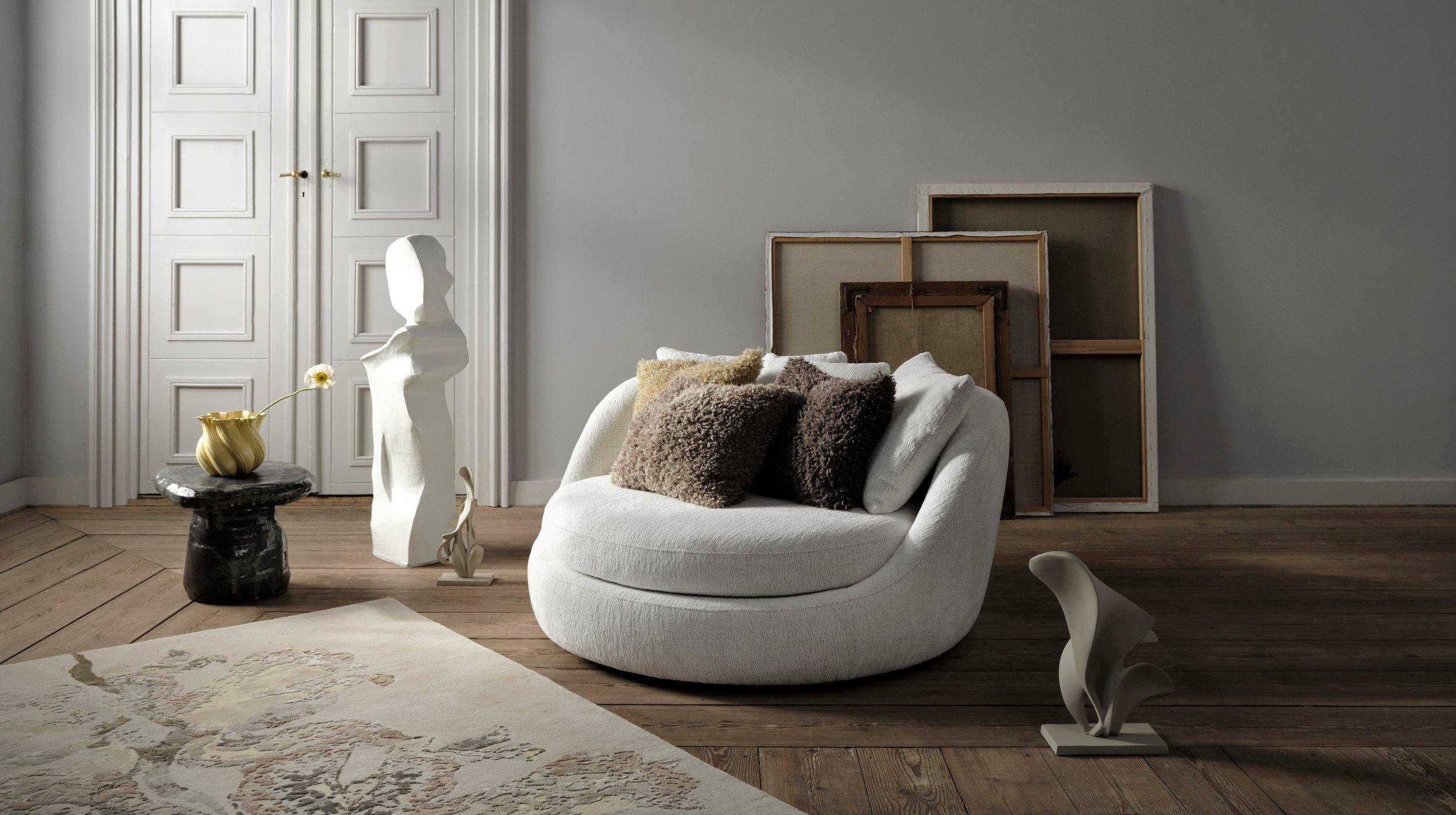 Stack of colorful pillows on a wooden chair in a sunlit room. A hand is adding an orange pillow to the top.
