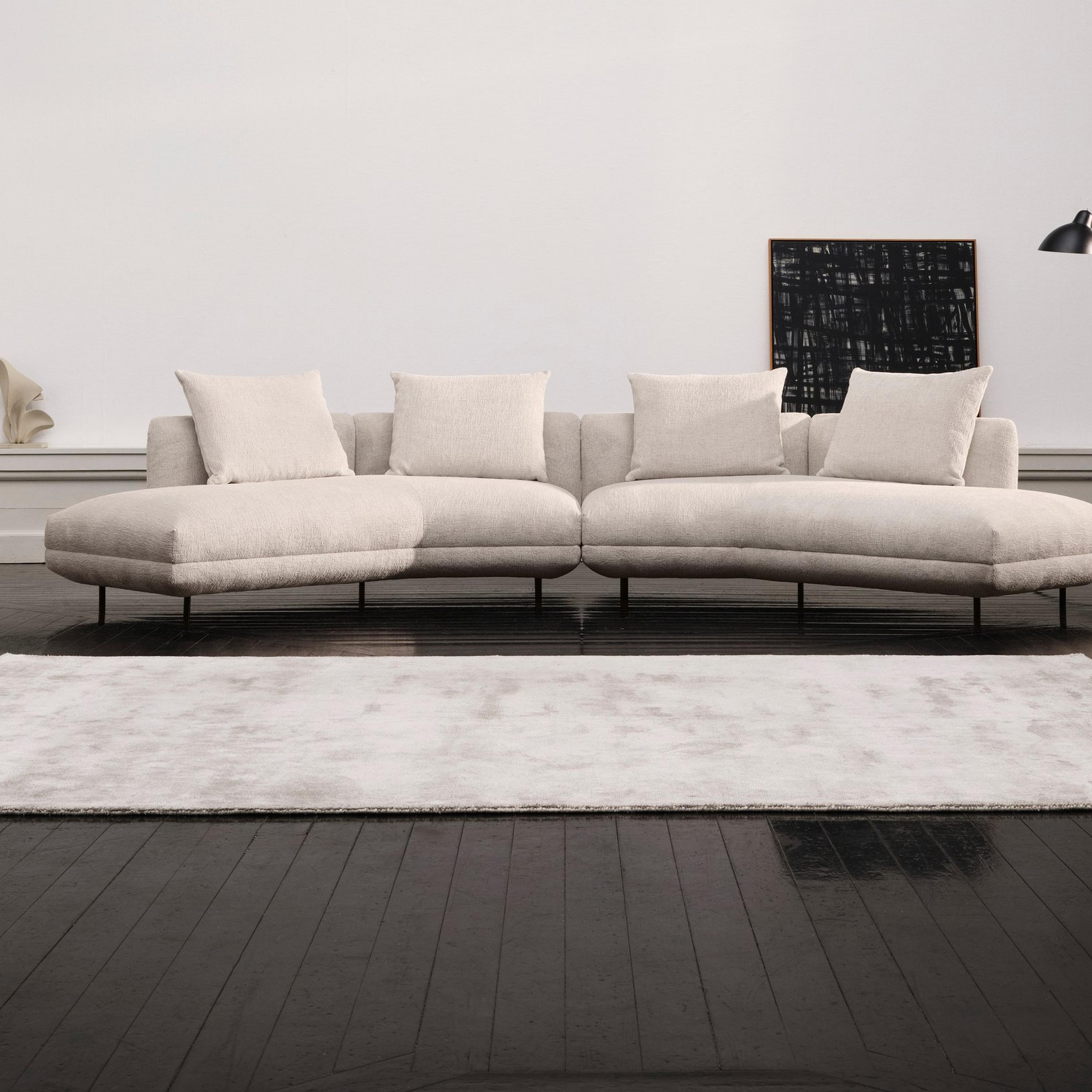Modern living room with a beige curved sofa, black chair, floor lamp, and abstract art.