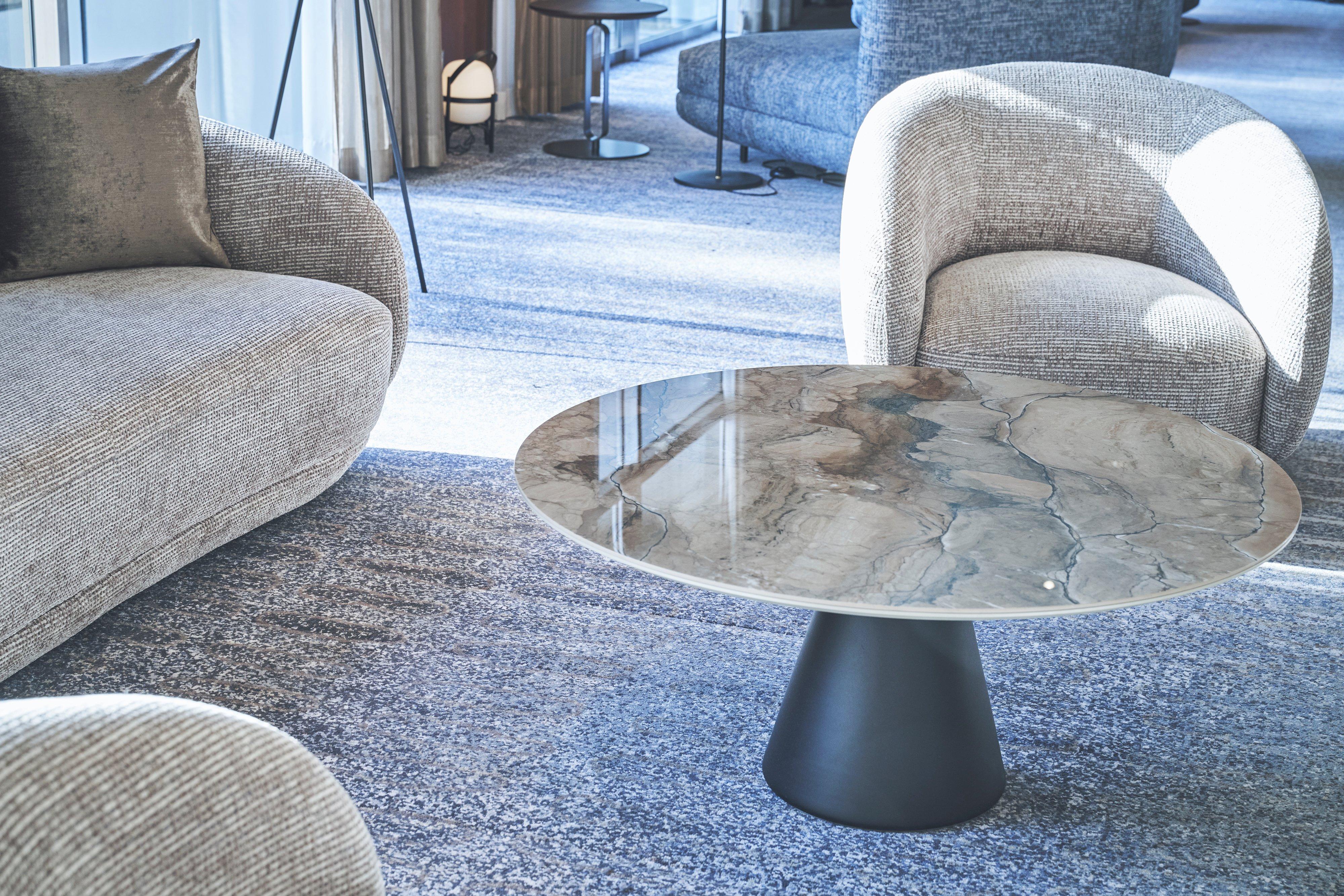 Round marble-effect coffee table with black pedestal base between upholstered armchairs.