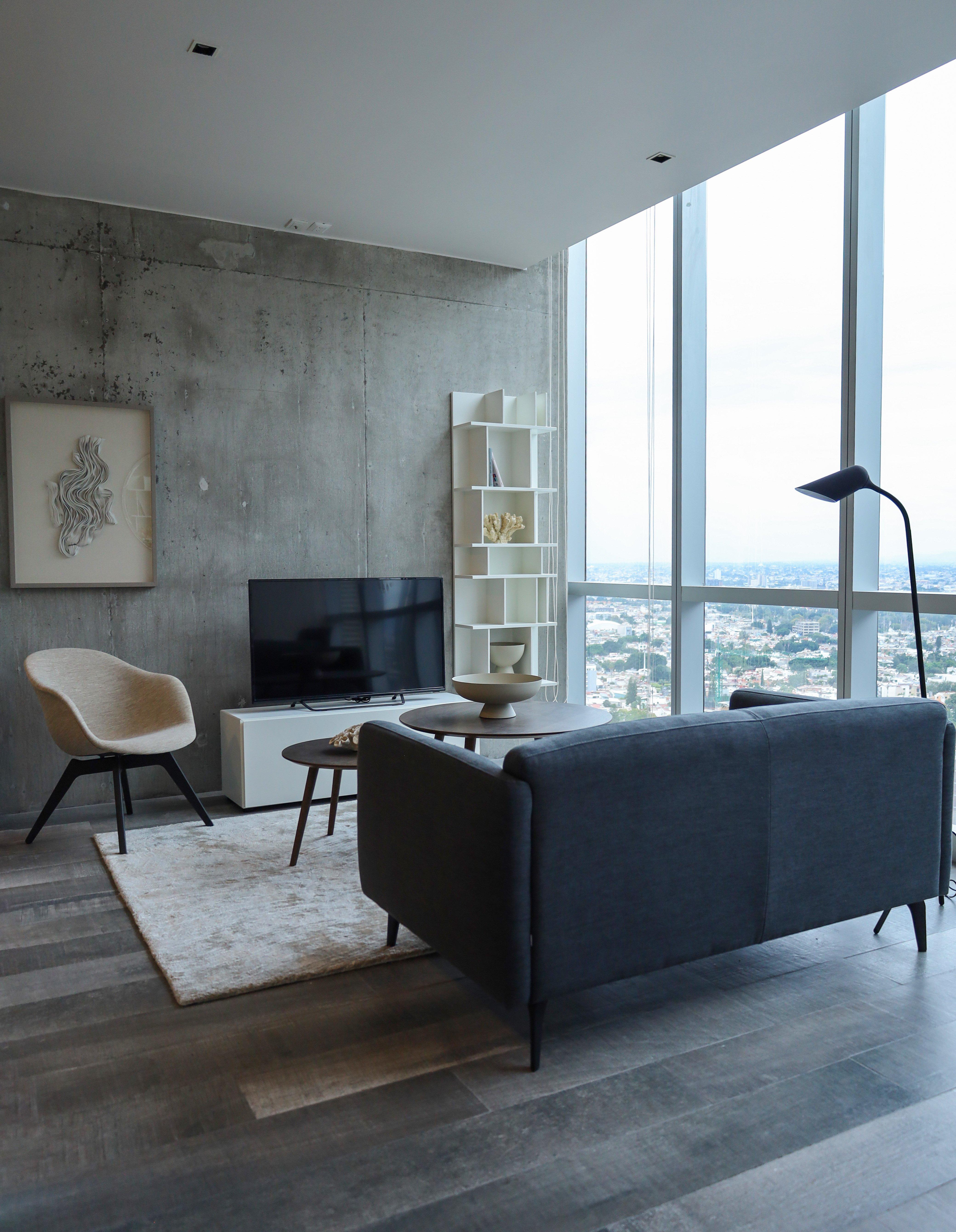 Modern living room with grey sofa, TV, armchair, and large windows.