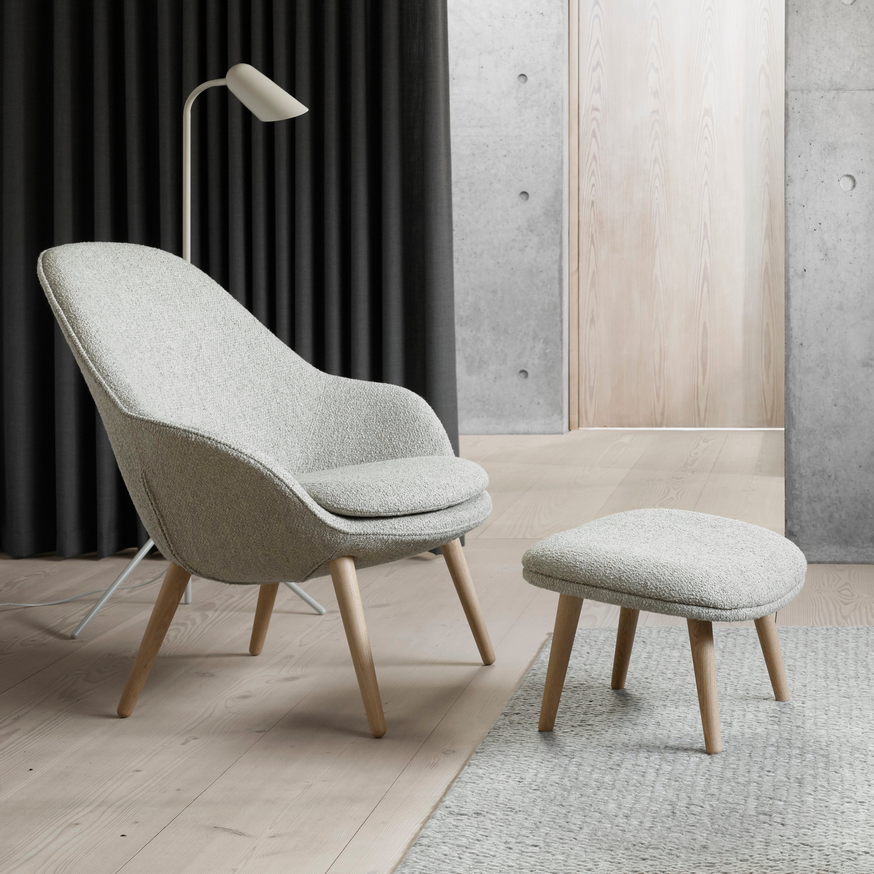 Modern stol med matchande fotpall, golvlampa, mörka gardiner och accenter i betong.