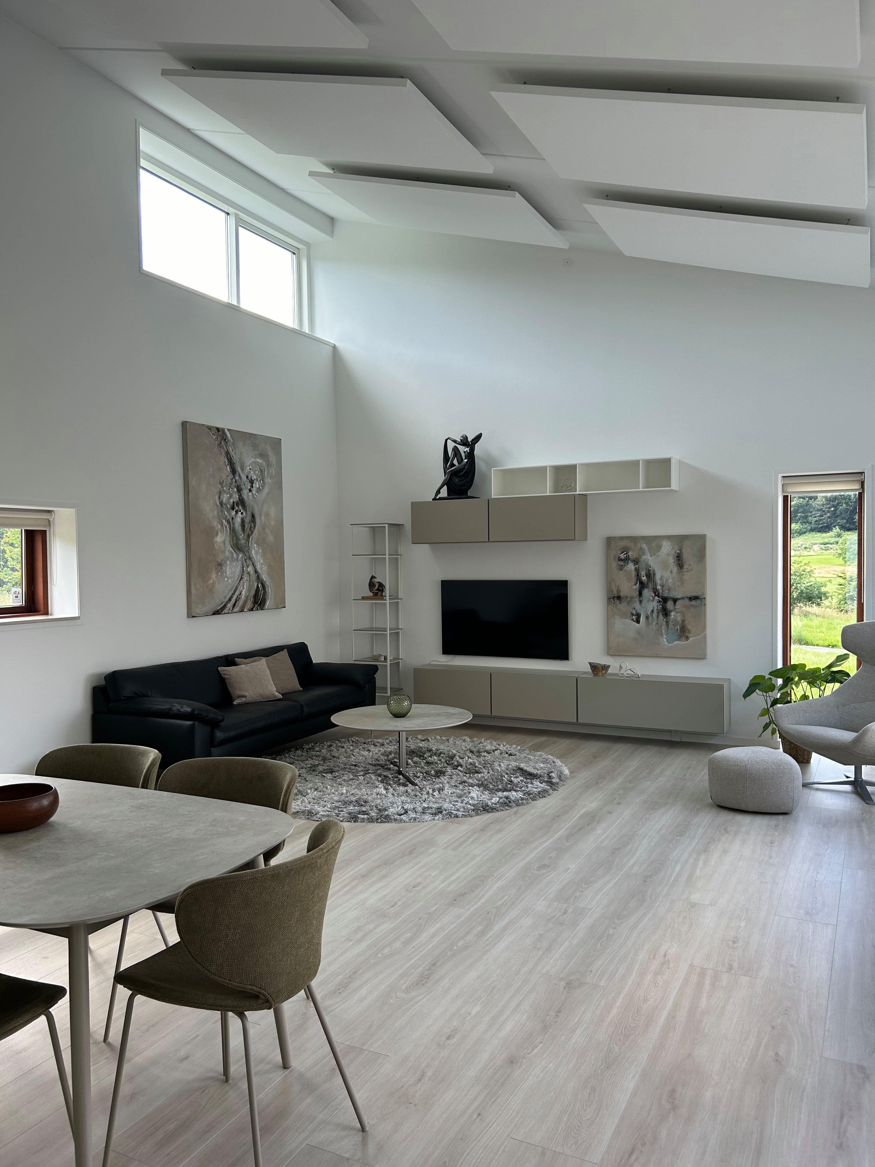Minimalist living room with wall-mounted cabinets, a flat-screen TV, abstract art, and a round table on a textured grey rug.