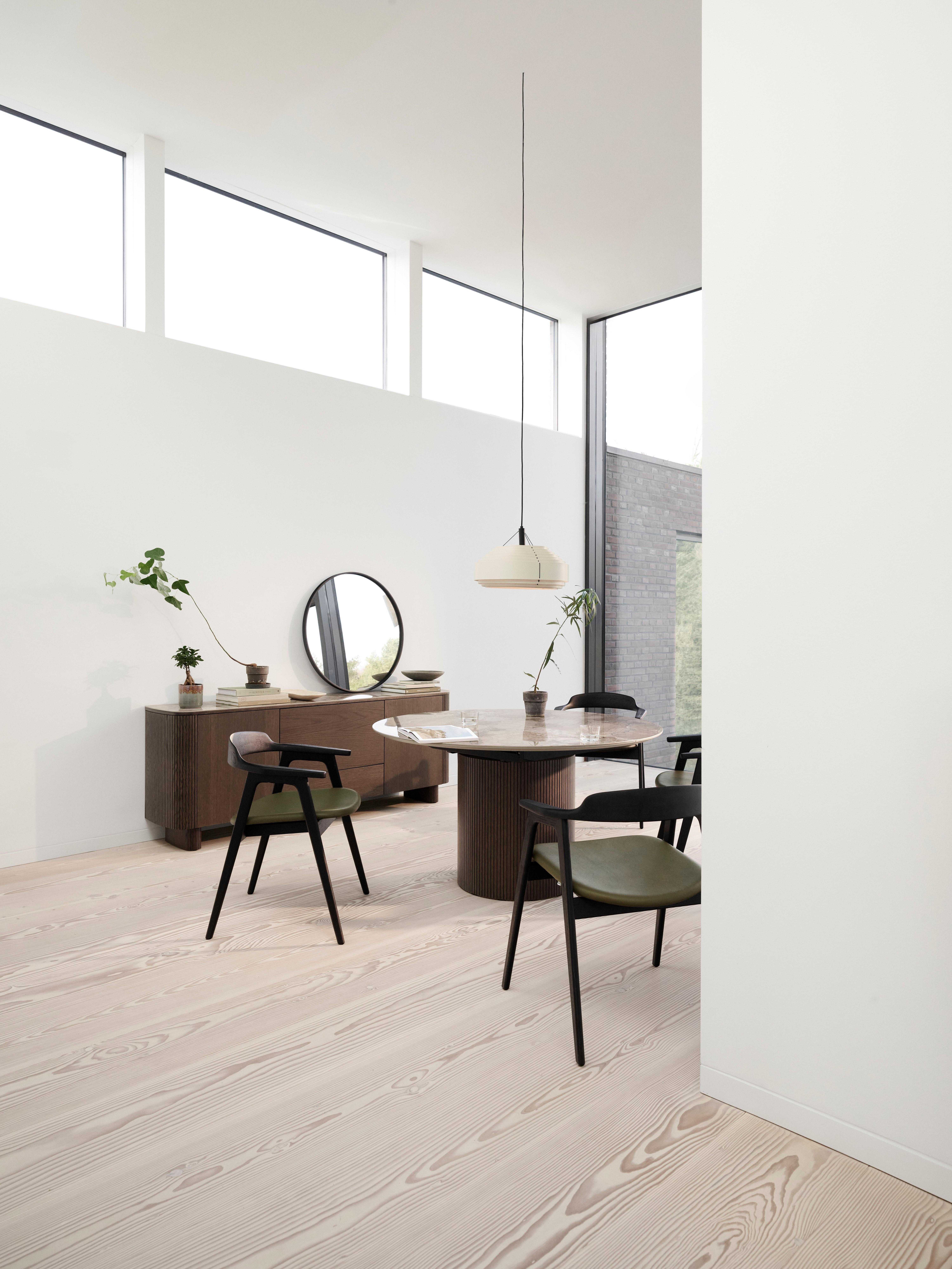 Minimalist dining room featuring a Santiago extendable dining table with a marble top, Santiago sideboard, and Seoul dining chairs with green cushions. Decor includes a Bubble vase, Ribbon vase, and a Paddle pendant light. The room has a round mirror on the sideboard and large windows.