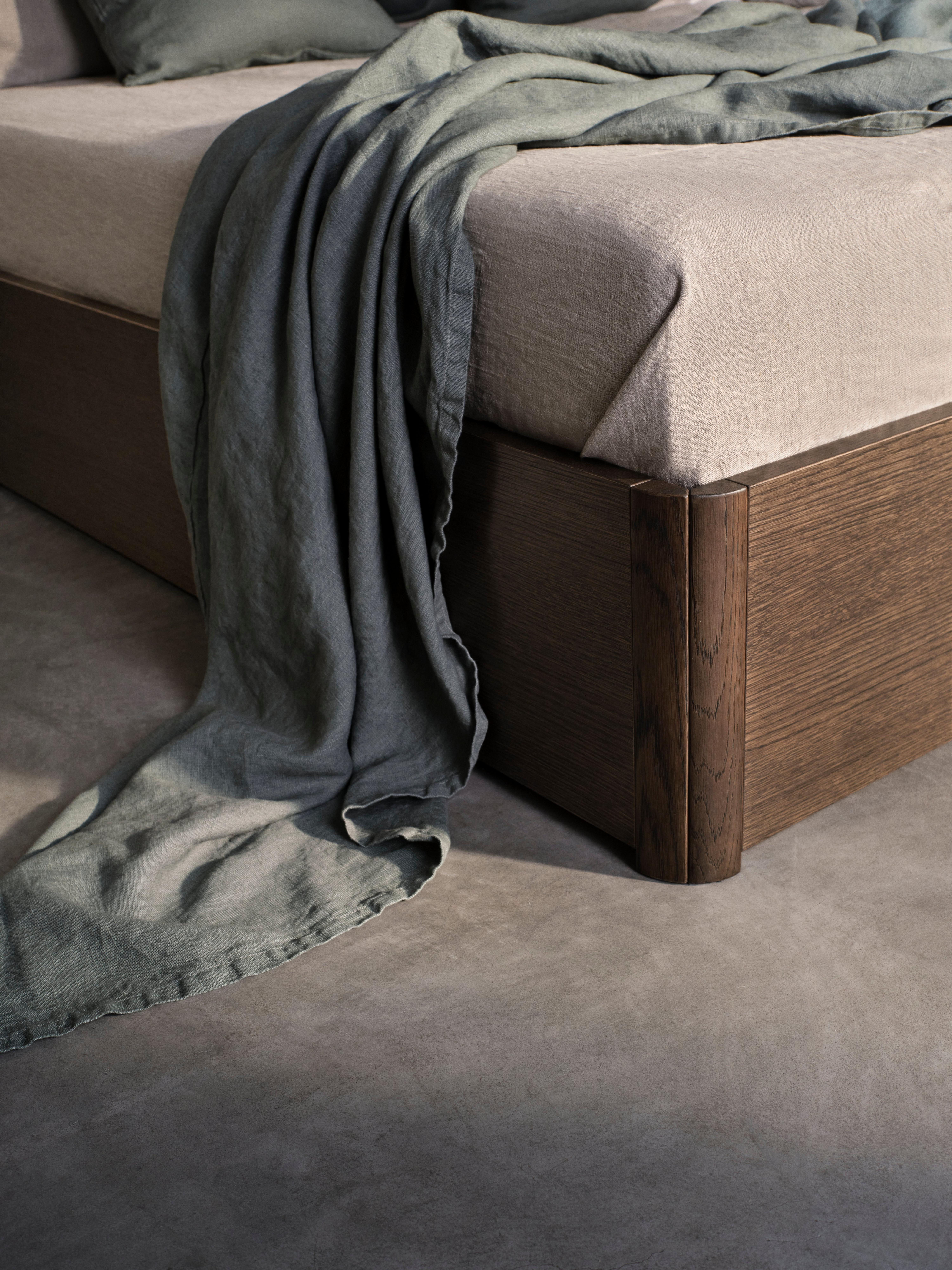 Unmade bed with green bedspread draping down on the floor