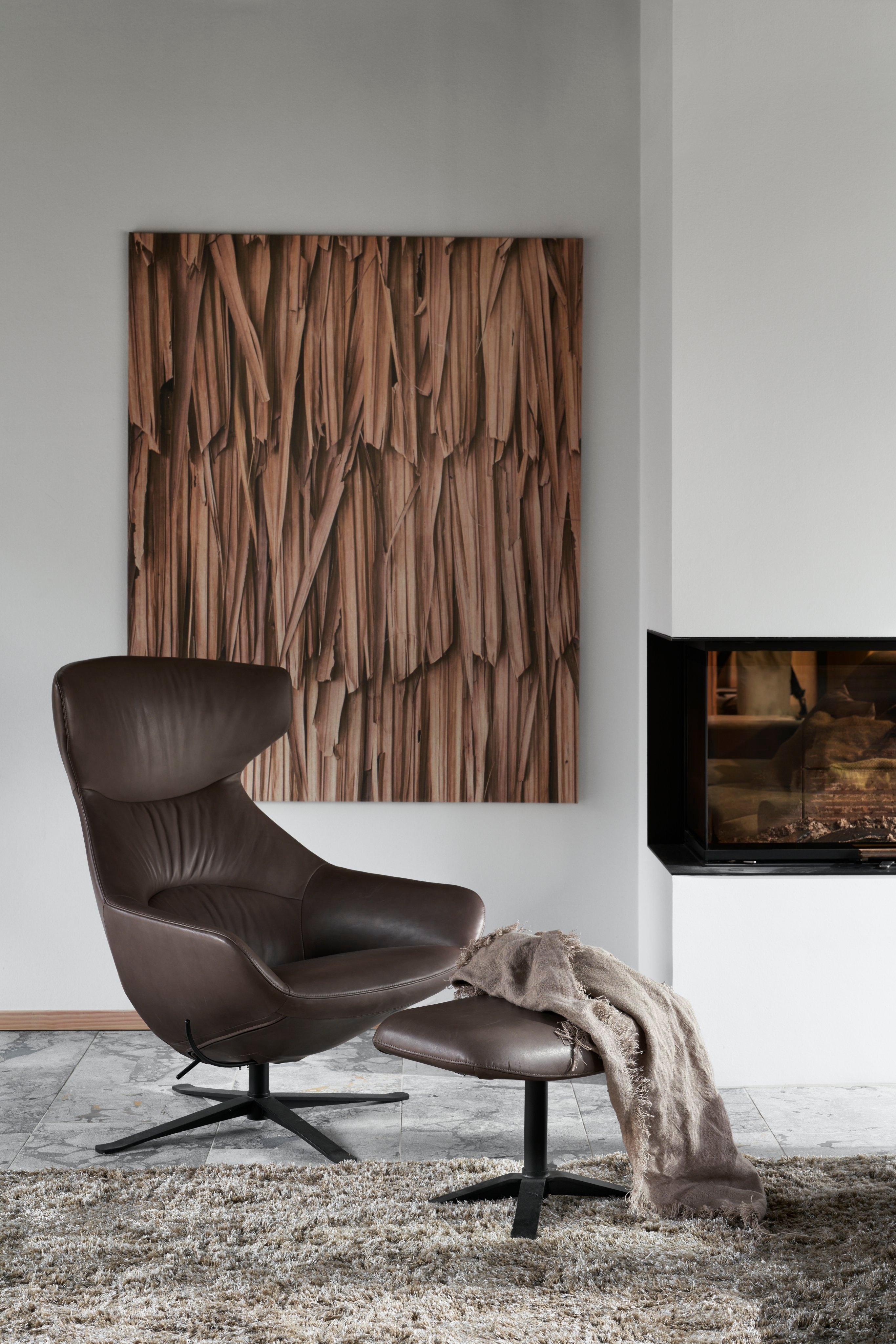 Moderna silla de piel marrón con puf, alfombra peluda, arte de madera y chimenea.