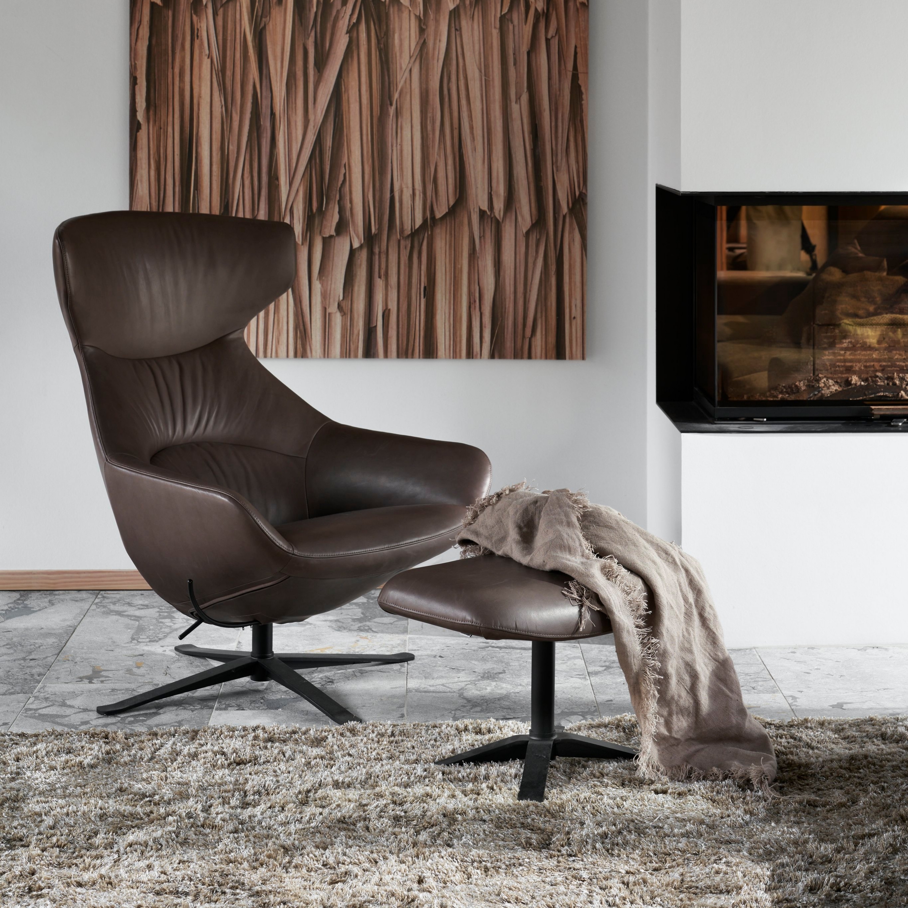 现代棕色皮革椅，配备脚凳、沙发地毯、木制画和壁炉。