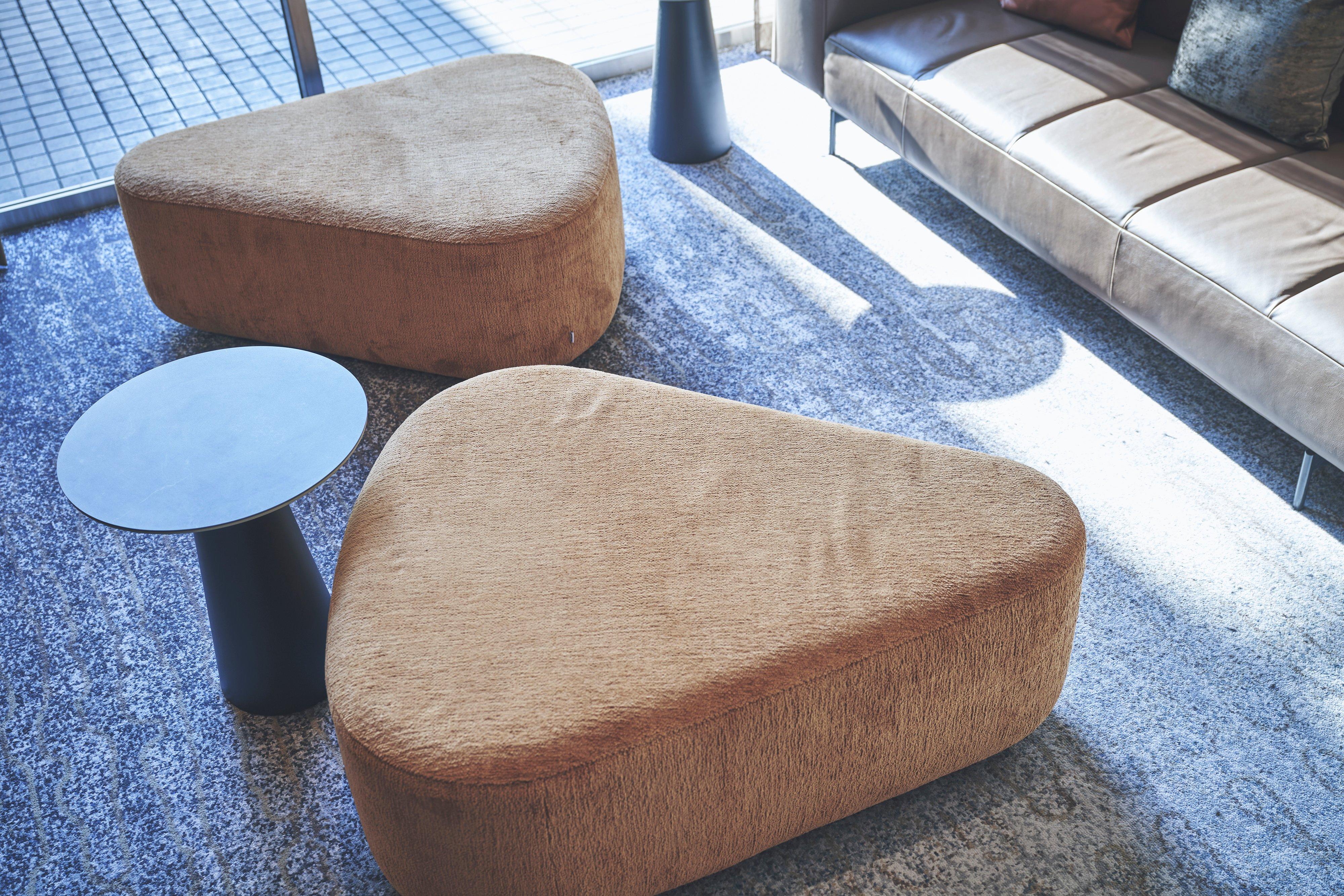 Two upholstered ottomans with a small round side table in a living room.