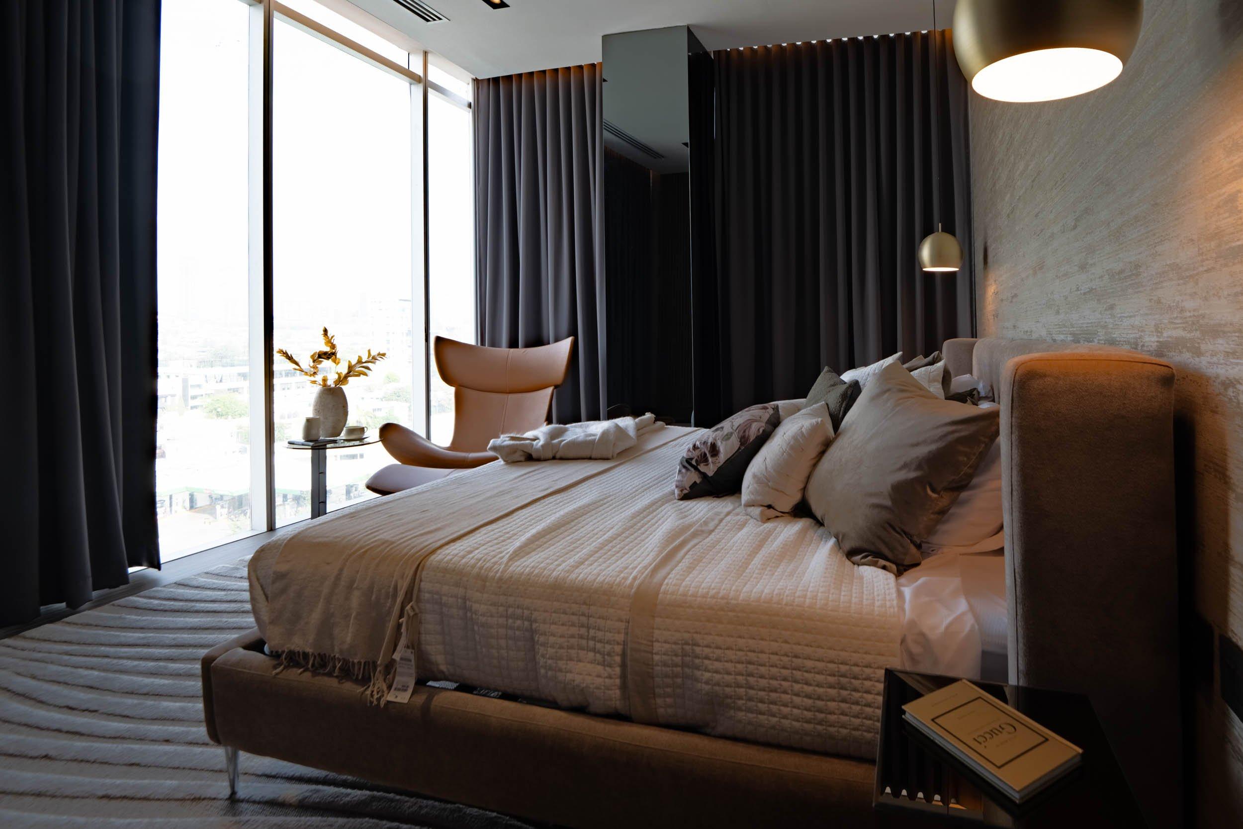 Chambre moderne avec grand lit, fauteuil, rideaux occultants et lampe suspendue près de la fenêtre.