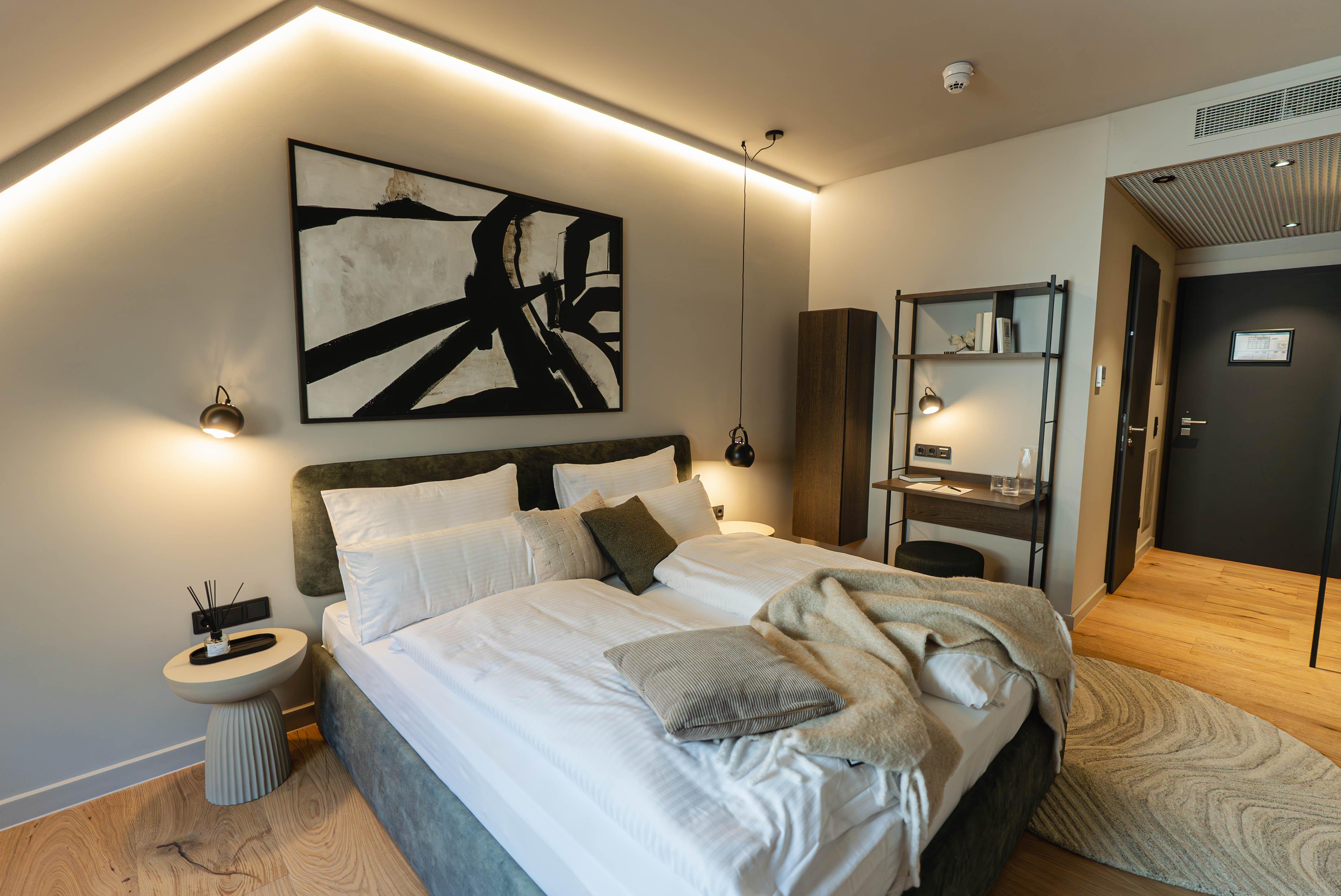 Chambre moderne avec lit double, tableau abstrait, bureau et étagères.