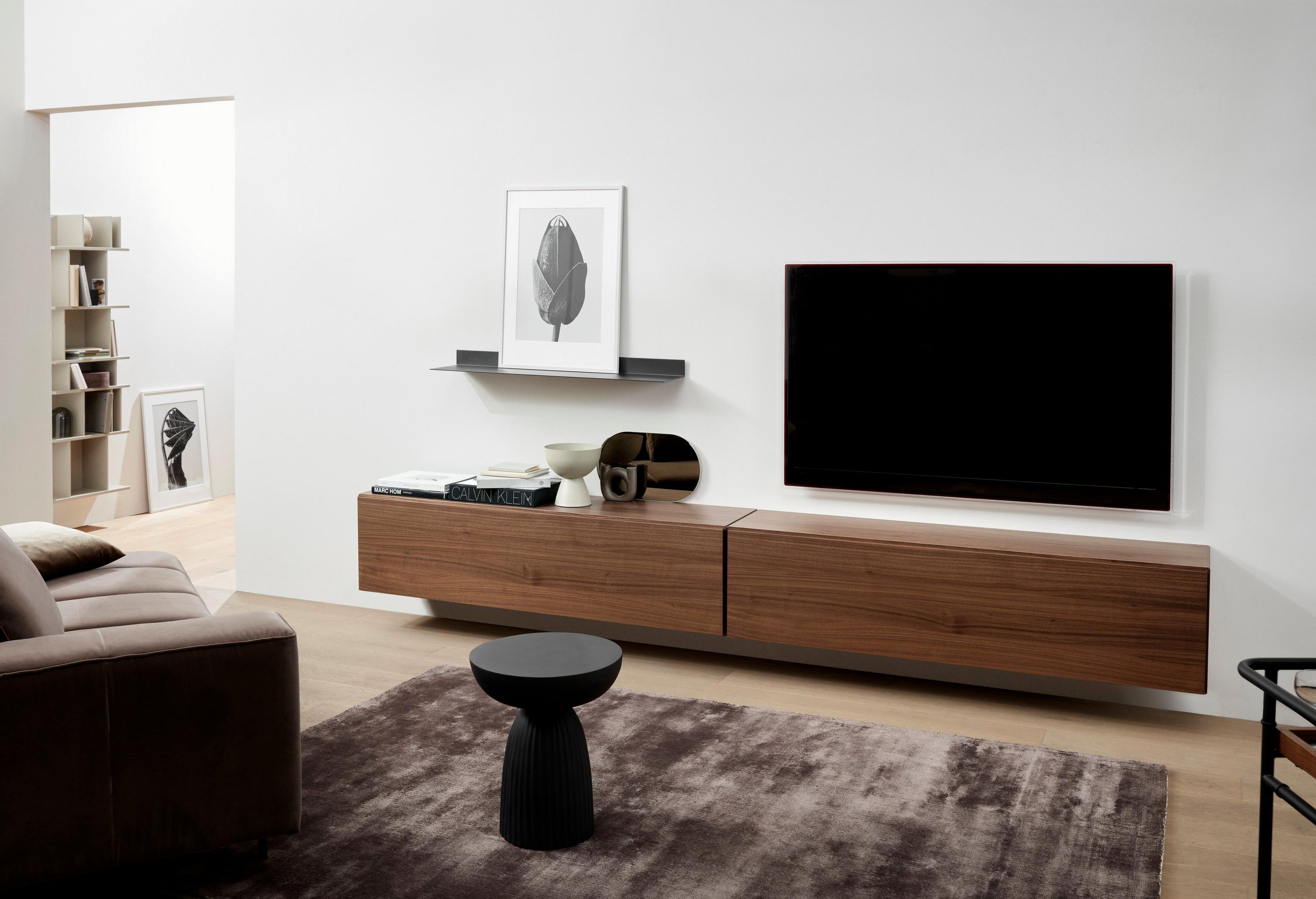 Modern living room with a wooden TV console, black stool, artwork, and a glimpse of a bookshelf.