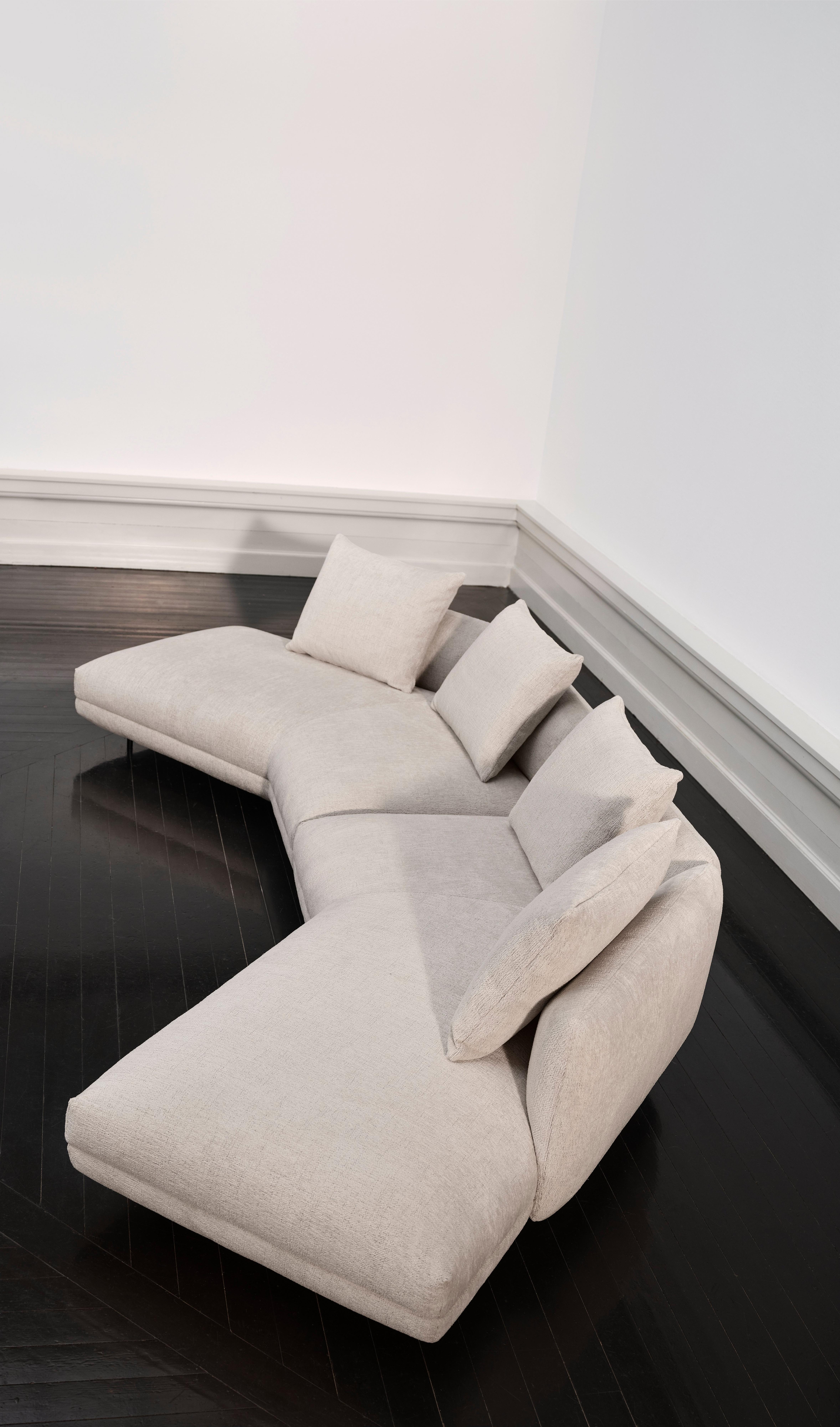 Sofá moderno em forma de L com almofadas cinza claro sobre piso de madeira escura.