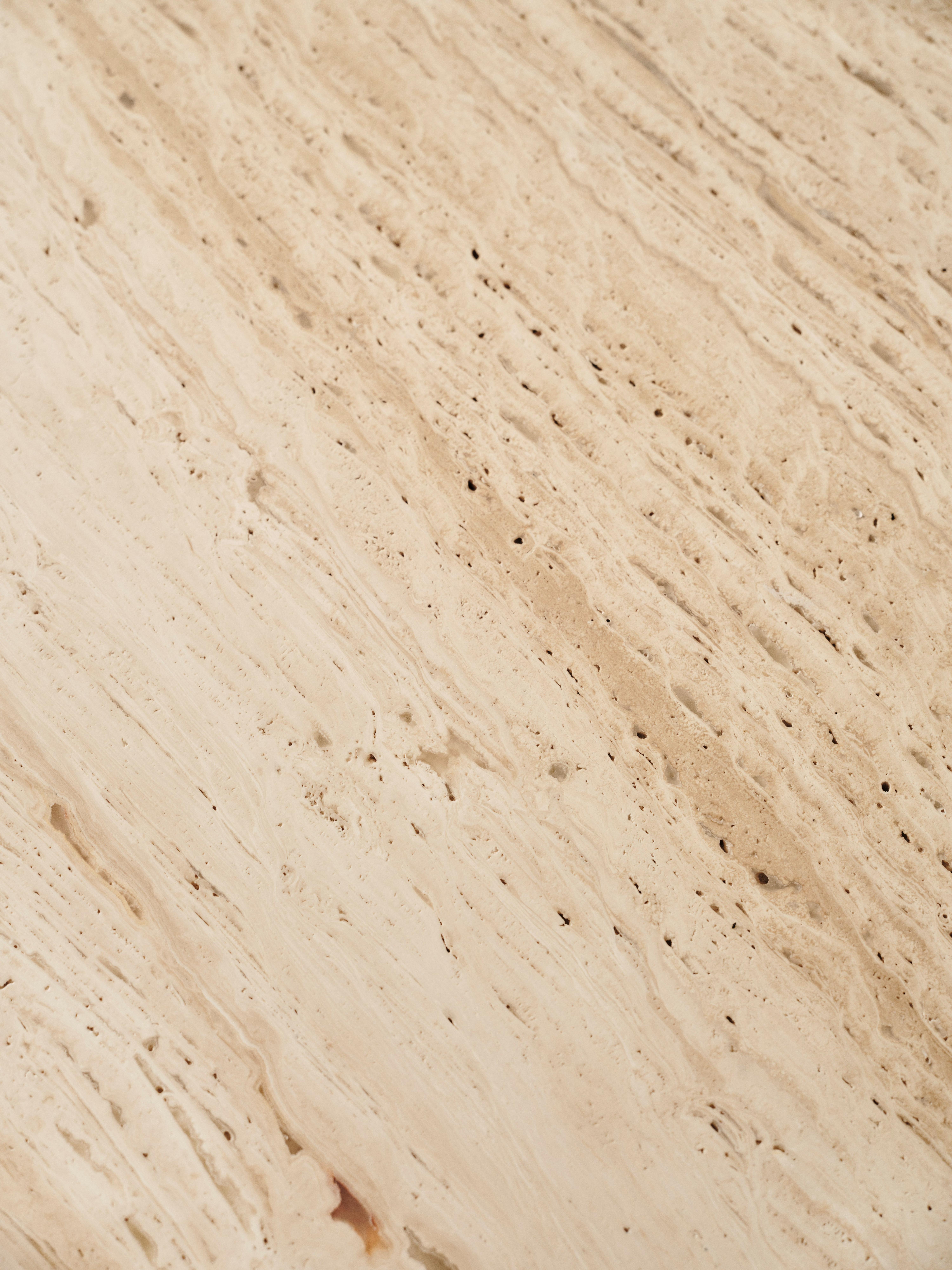 Nahaufnahme einer beigen, strukturierten Steinoberfläche mit natürlichen Linien und Poren.