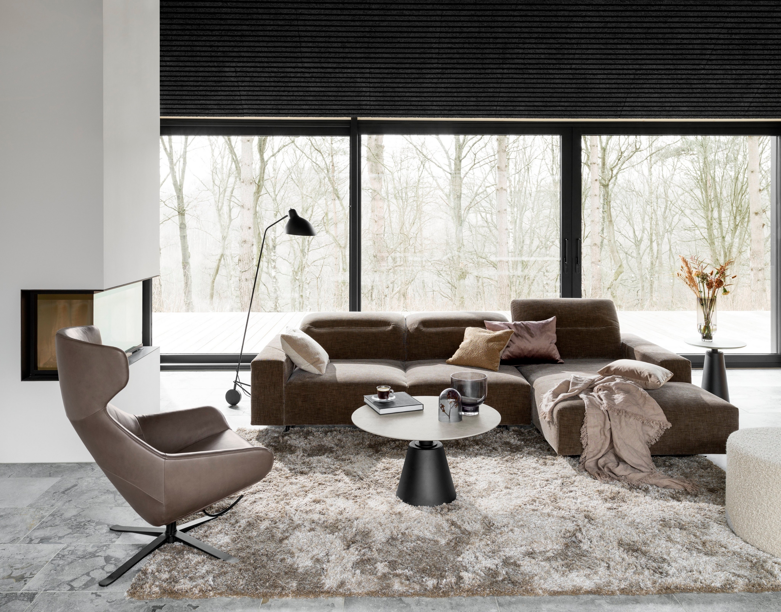 Un salon moderne avec un canapé modulable marron, un tapis gris et un lampadaire noir près de la fenêtre.