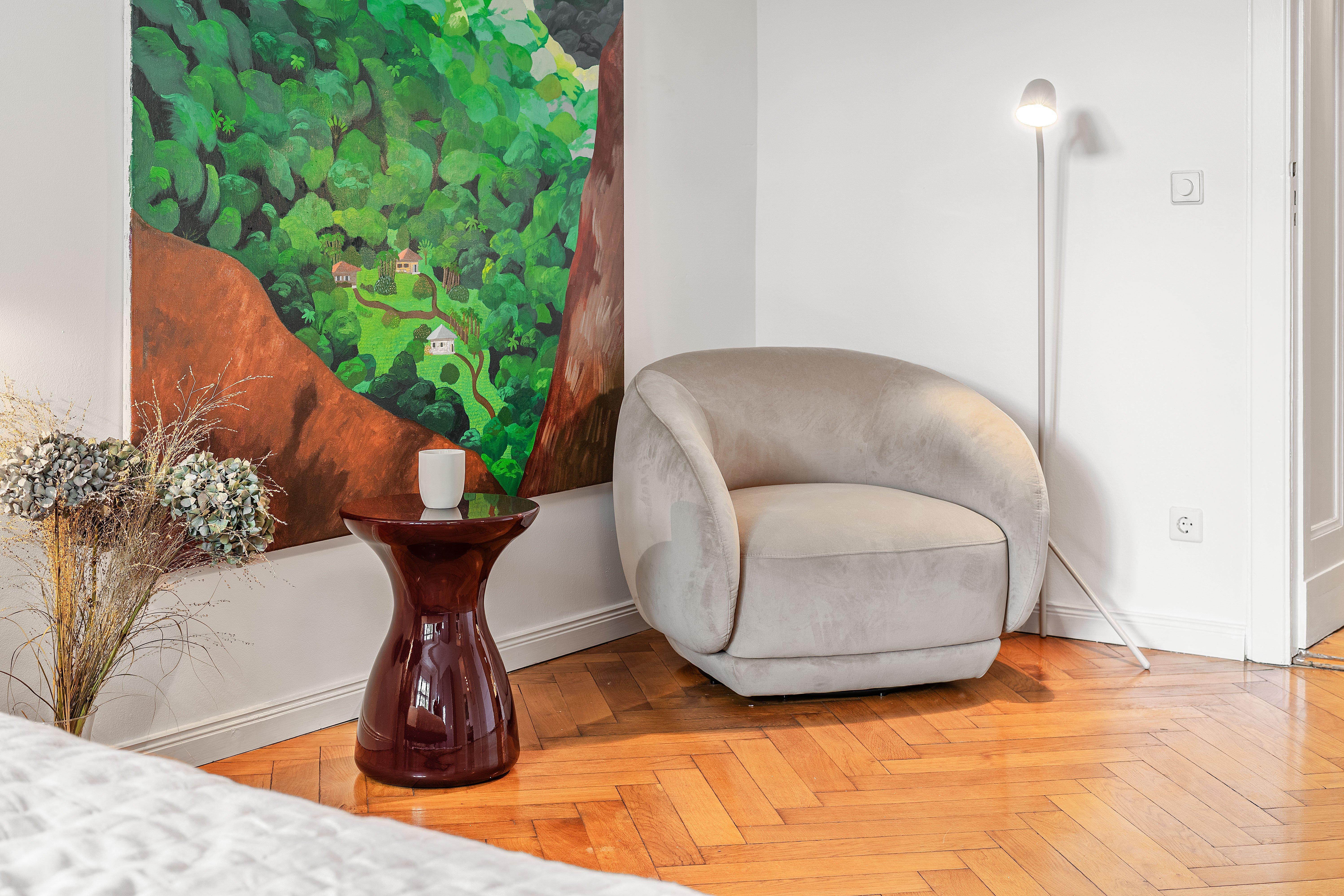 Fauteuil gris près d'une table avec tasse, lampe sur pied, tableau nature.