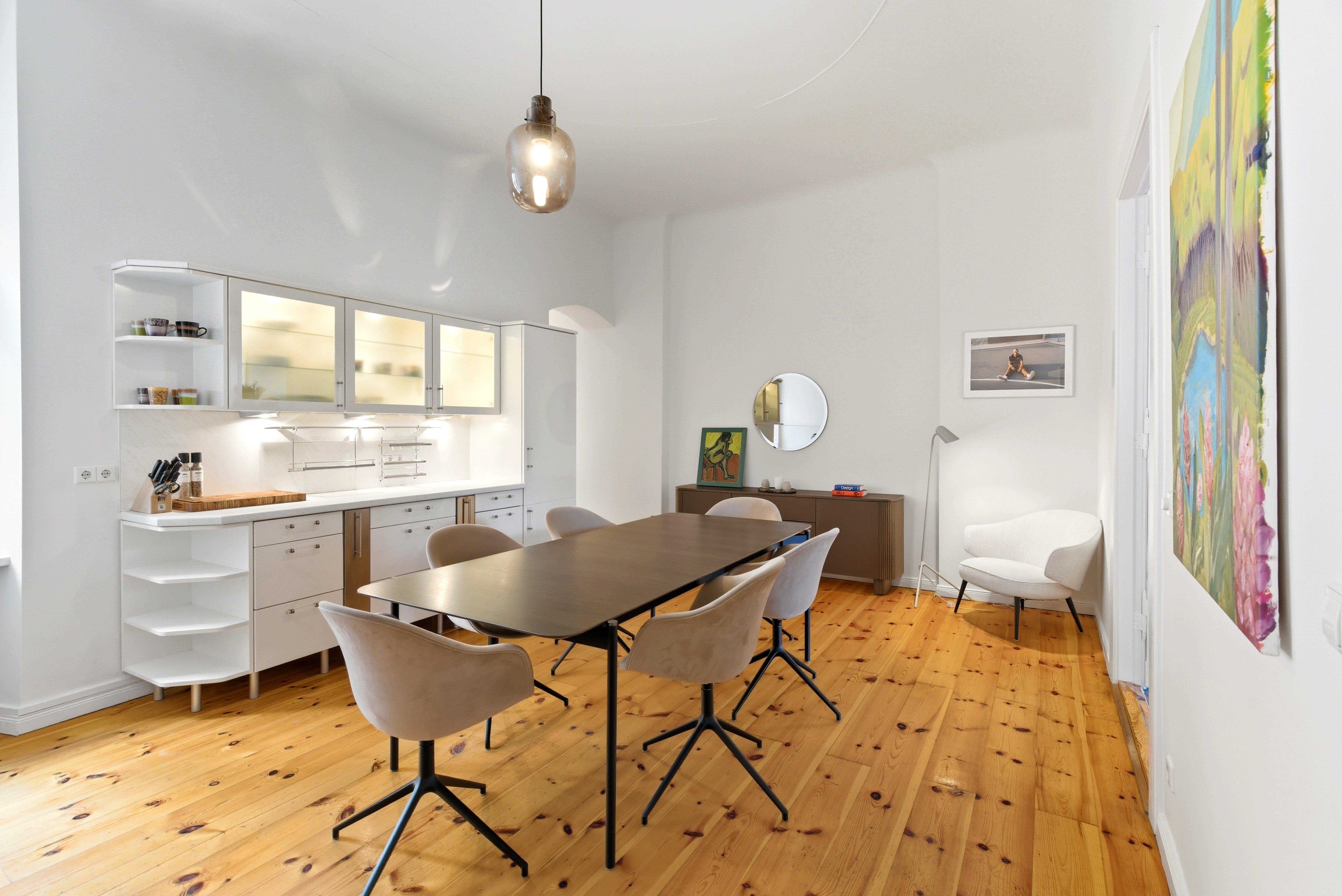 Salle à manger moderne avec table, chaises, cuisine blanche et lampadaire.
