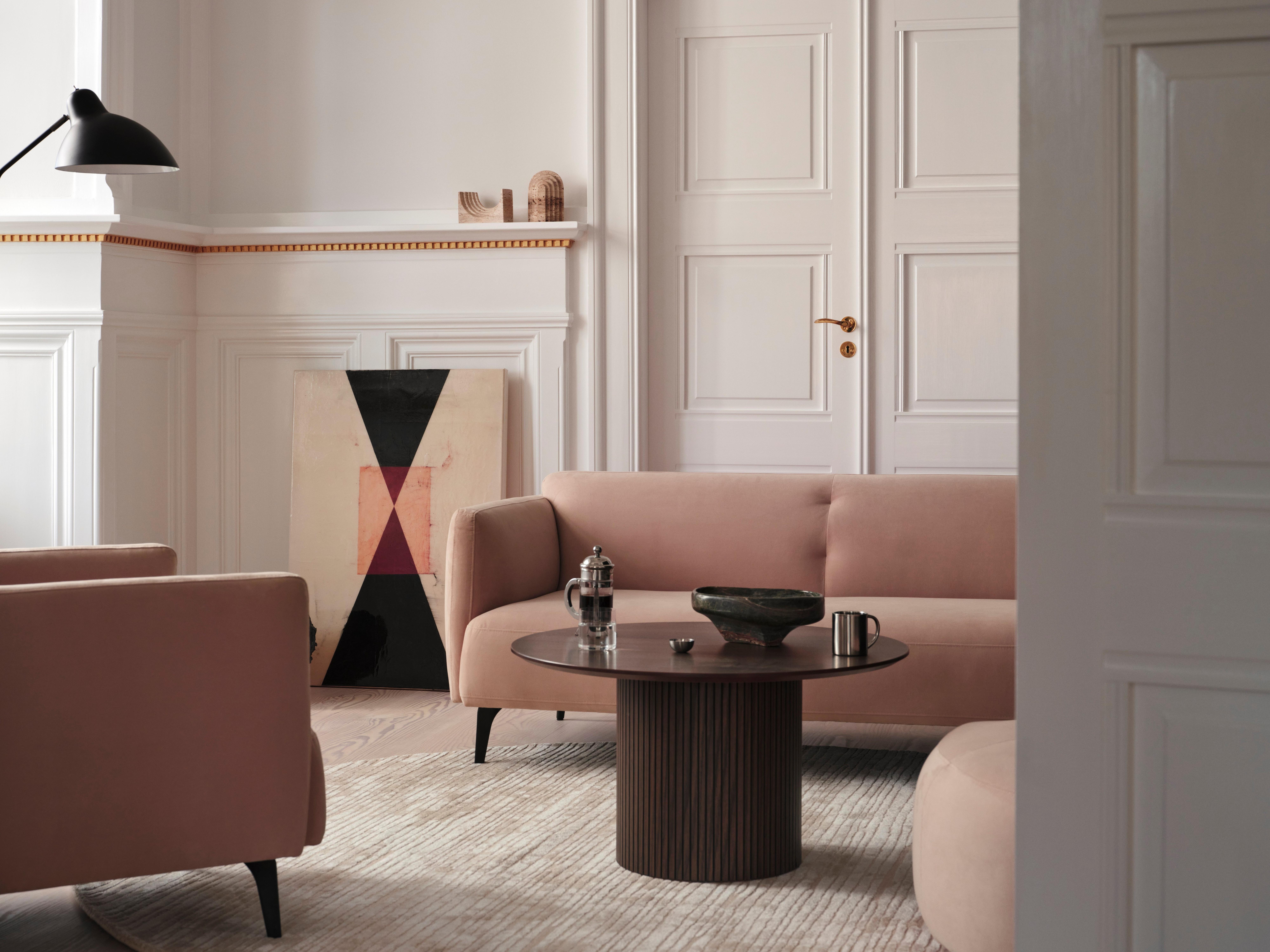 Modern living room with pink sofas, round coffee table, abstract art, and wall lamp.