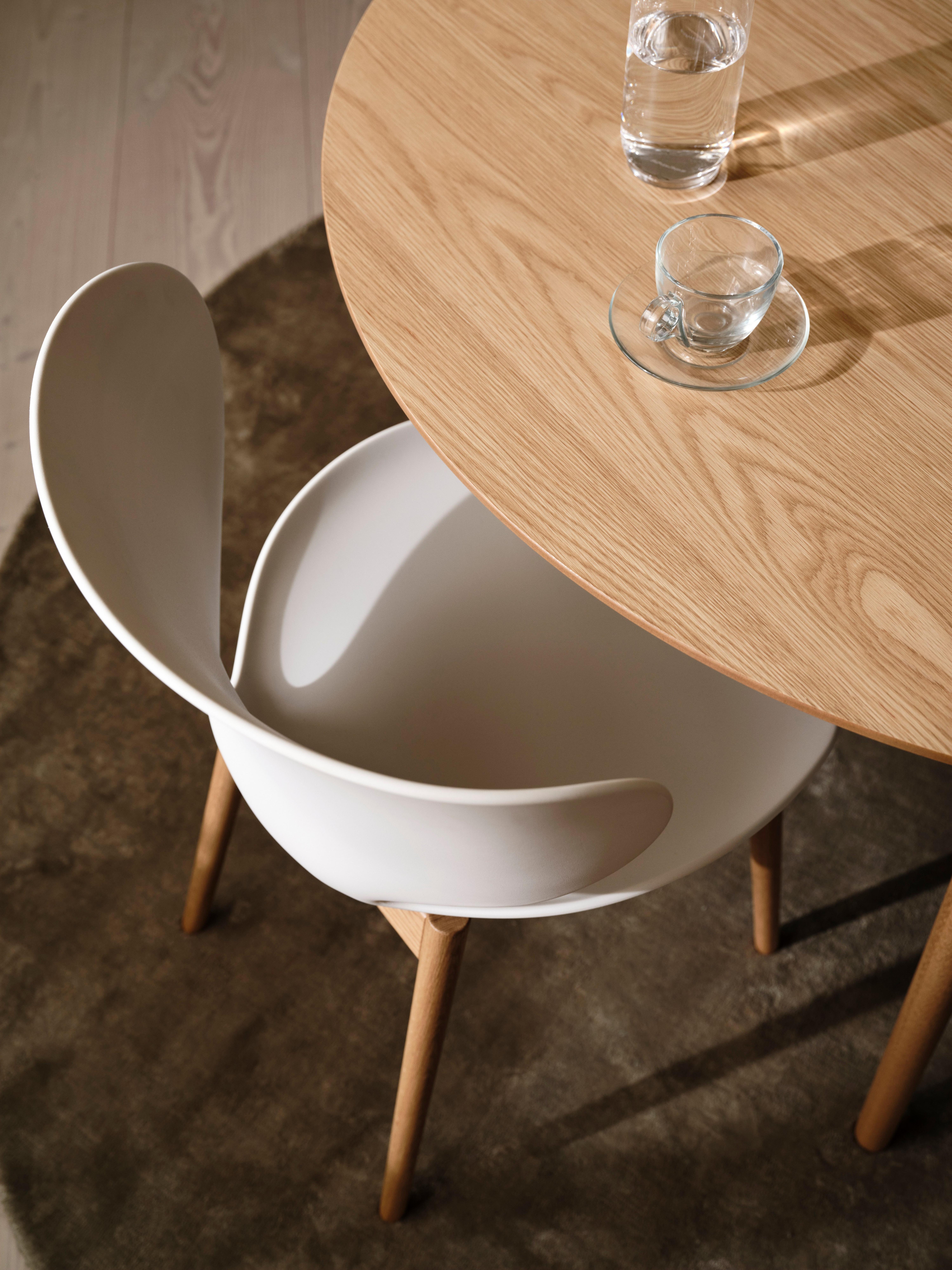 Wooden table with glass cup and water. White chair with wooden legs.